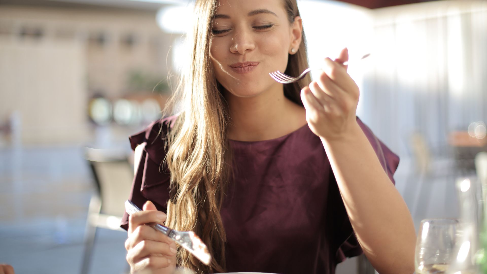 A woman savoring her meal with a smile, dining outdoors in a pleasant setting.