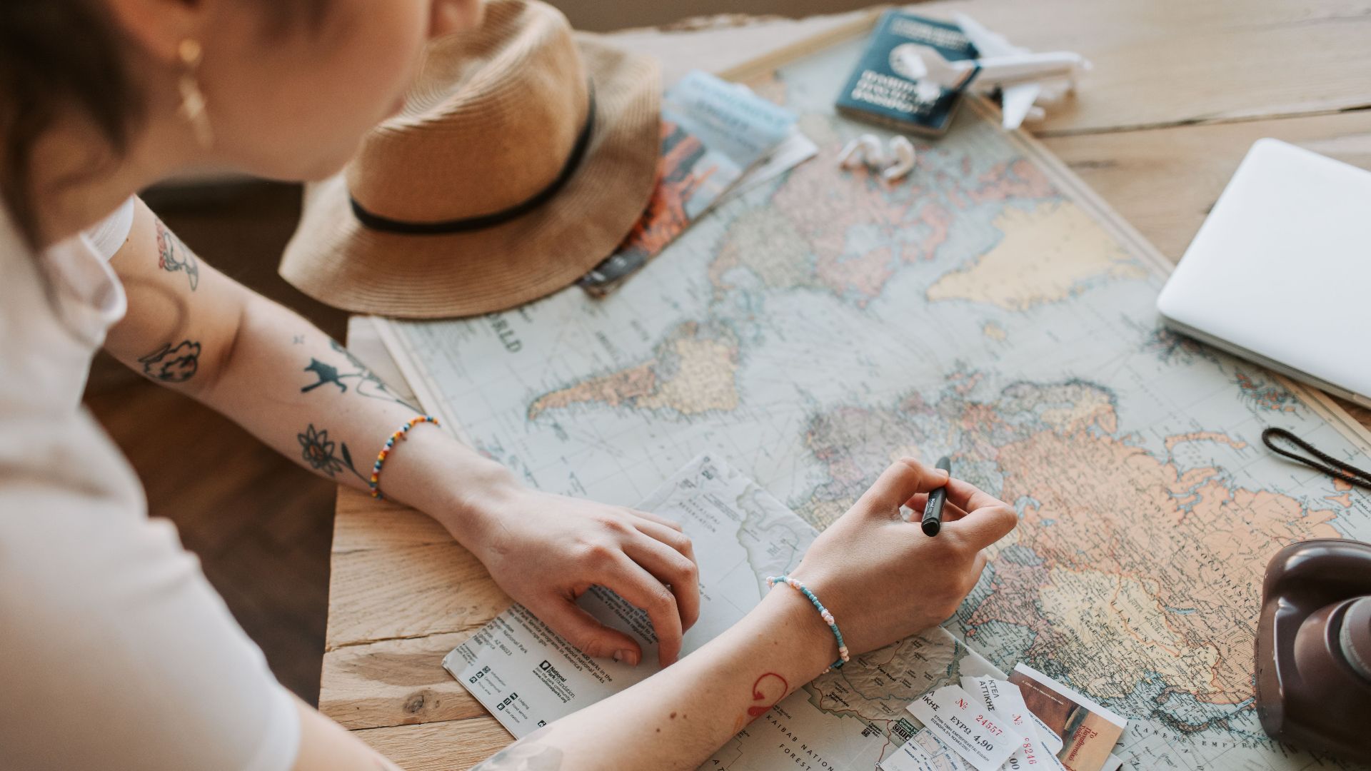 Person planning a journey with a map, passport, and travel essentials on a wooden table.