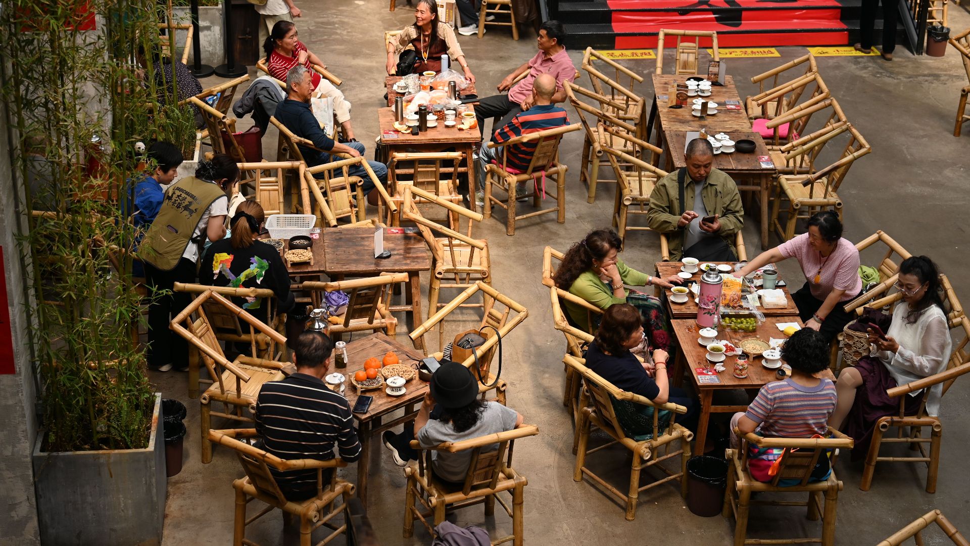 Overhead view of an indoor café with patrons seated at bamboo tables, capturing lively discussions.