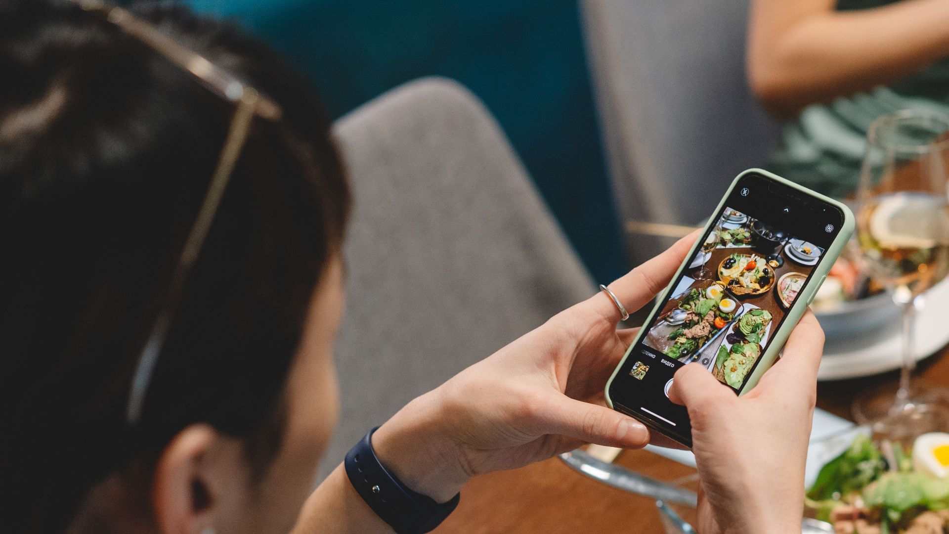 A person taking photos of a delicious dinner with wine, showcasing a vibrant dining scene indoors.