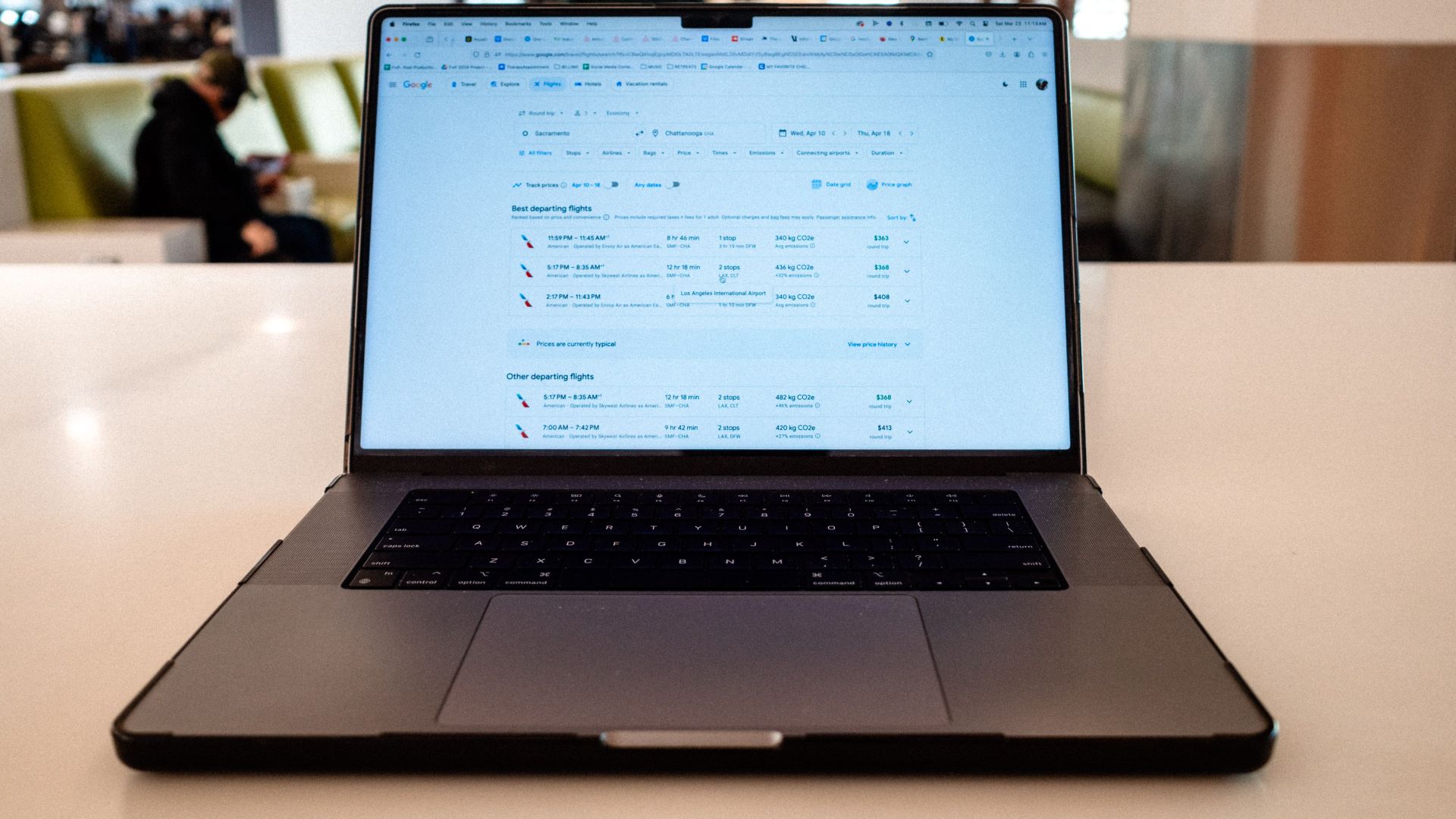A modern laptop displaying flight schedules on a white table in an airport lounge.