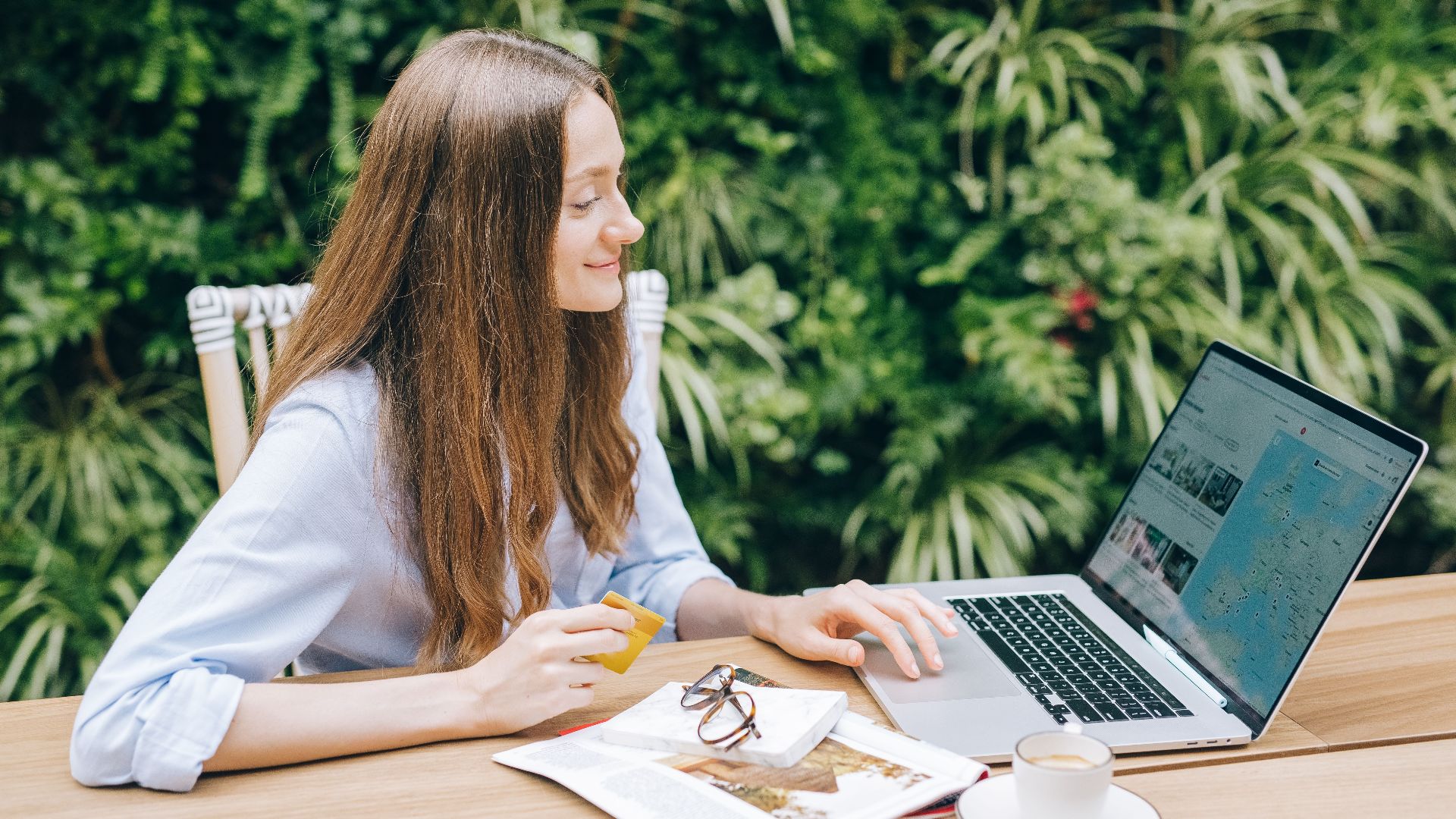 Young woman sitting at a table with a laptop and coffee, enjoying outdoor workspace.