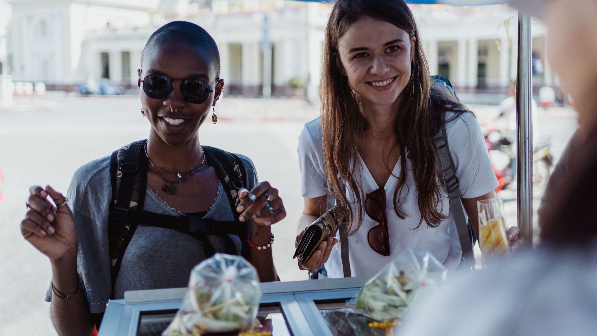 Two women enjoying street food at an outdoor market, exuding joy and travel spirit.