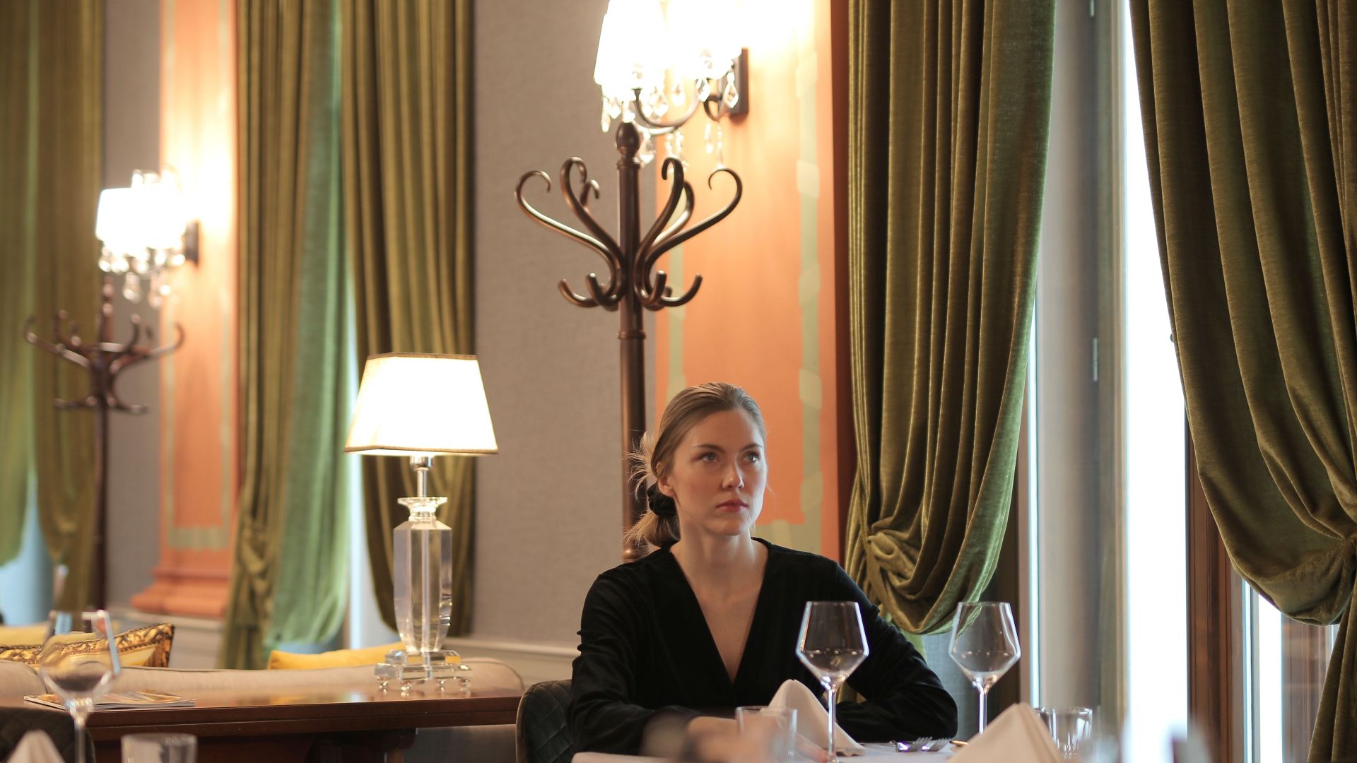 Woman sitting alone in a luxurious restaurant, surrounded by elegant decor and dim lighting.