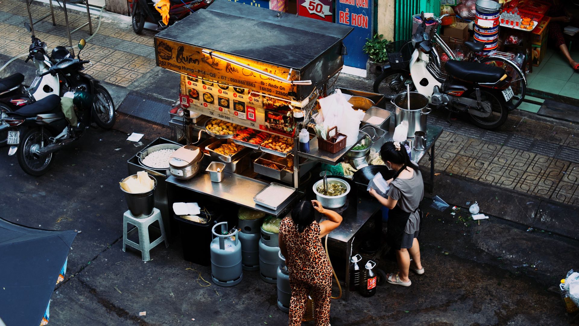 Two women preparing food at a bustling Vietnamese street food stall.