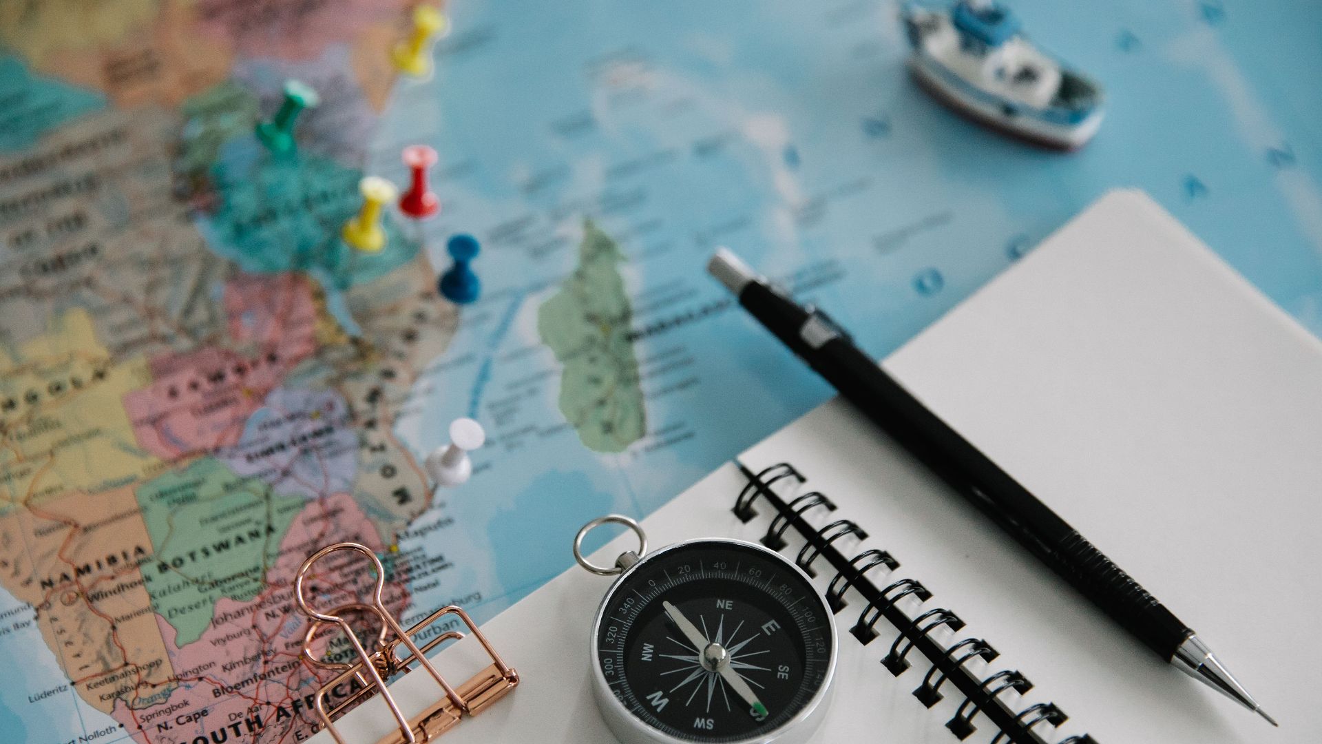 Flat lay of travel planning tools including a map, compass, notebook, and pen.