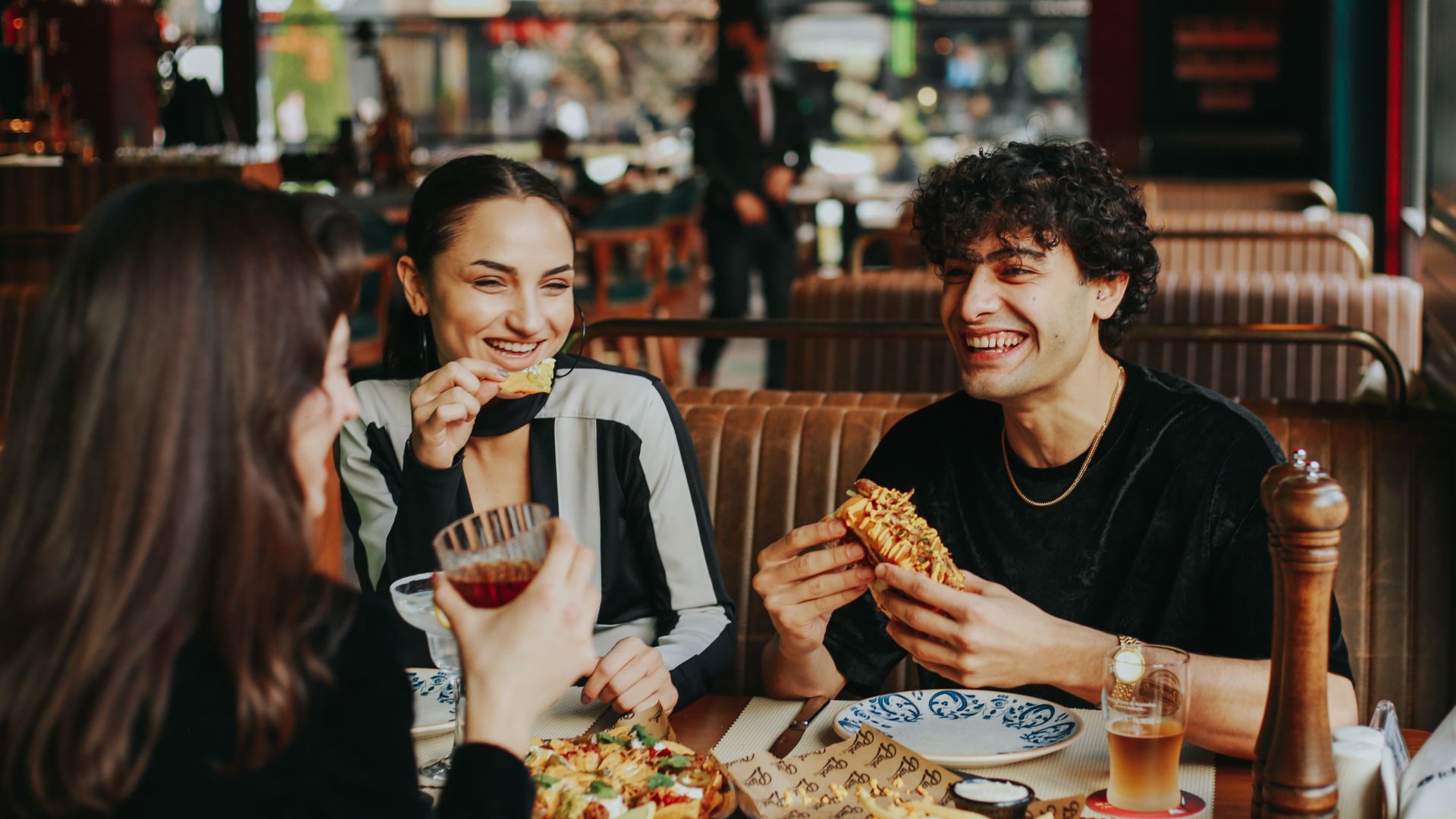 Group of friends laughing and eating at a restaurant, enjoying leisure time.
