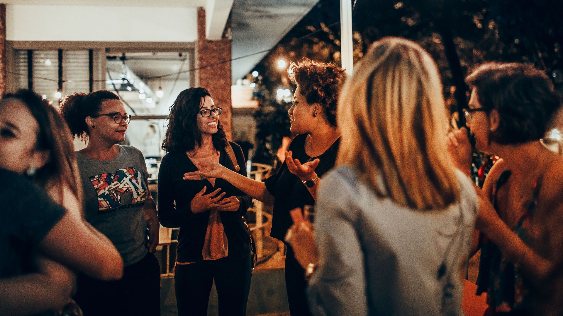 A vibrant group of women engaged in conversation during an outdoor evening gathering.