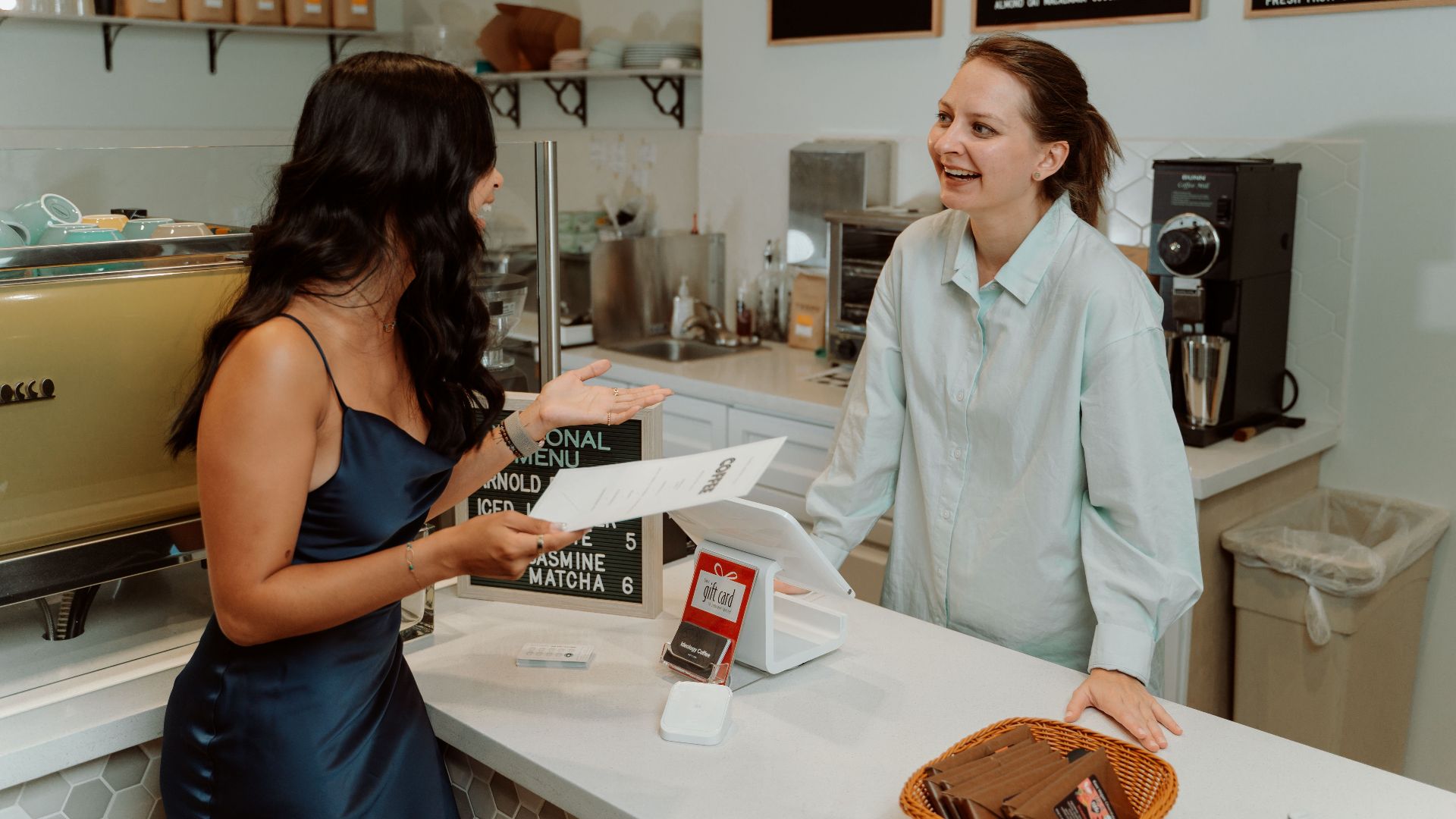Two women engaging in a cheerful conversation at a modern café counter.