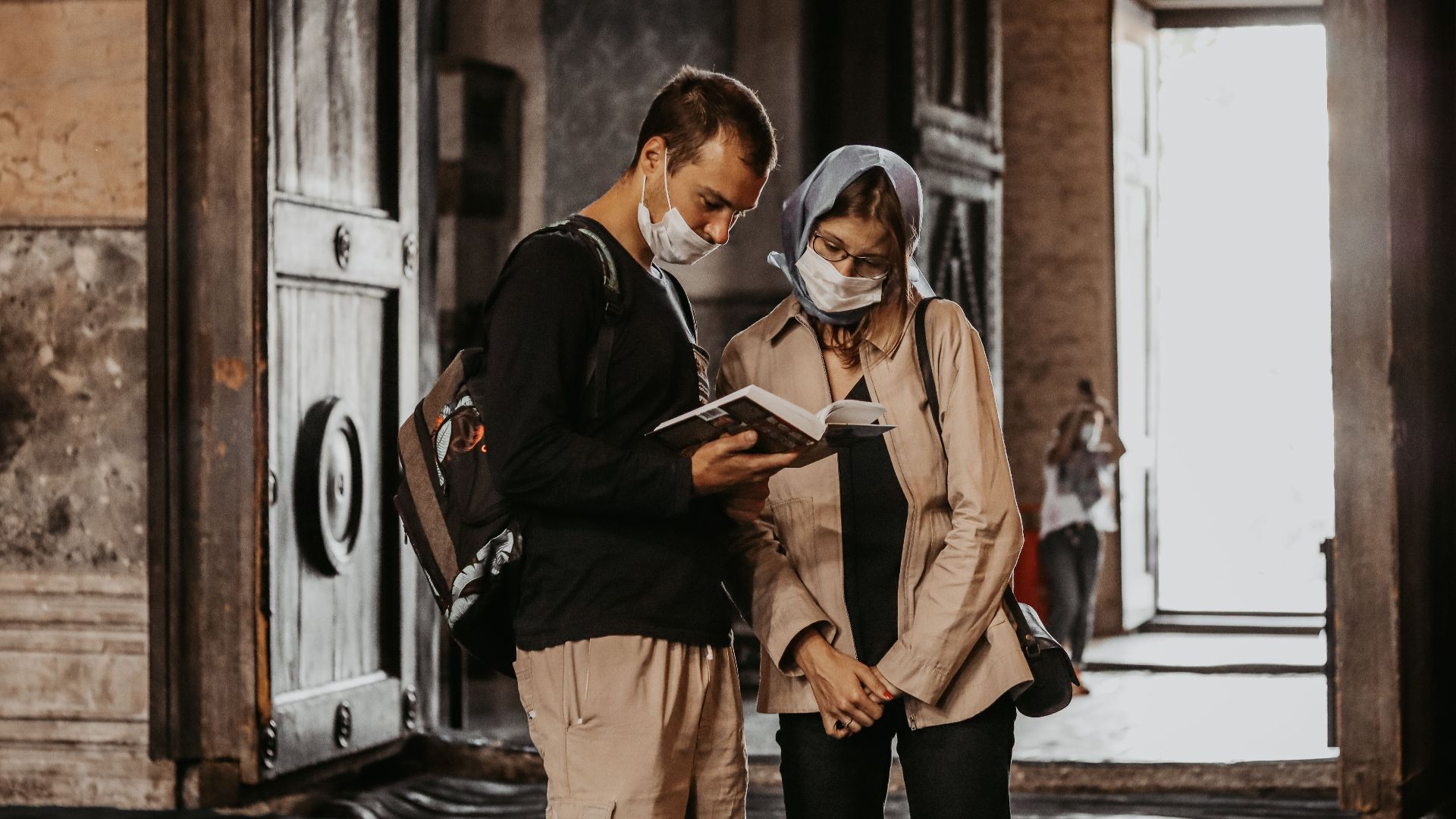 A couple wearing face masks reads a book together in a historic building.
