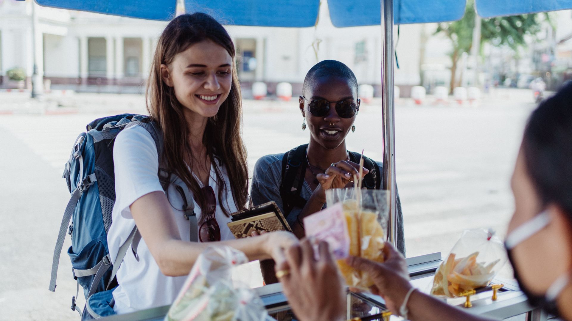 Travelers purchasing snacks from a street vendor at an outdoor market.