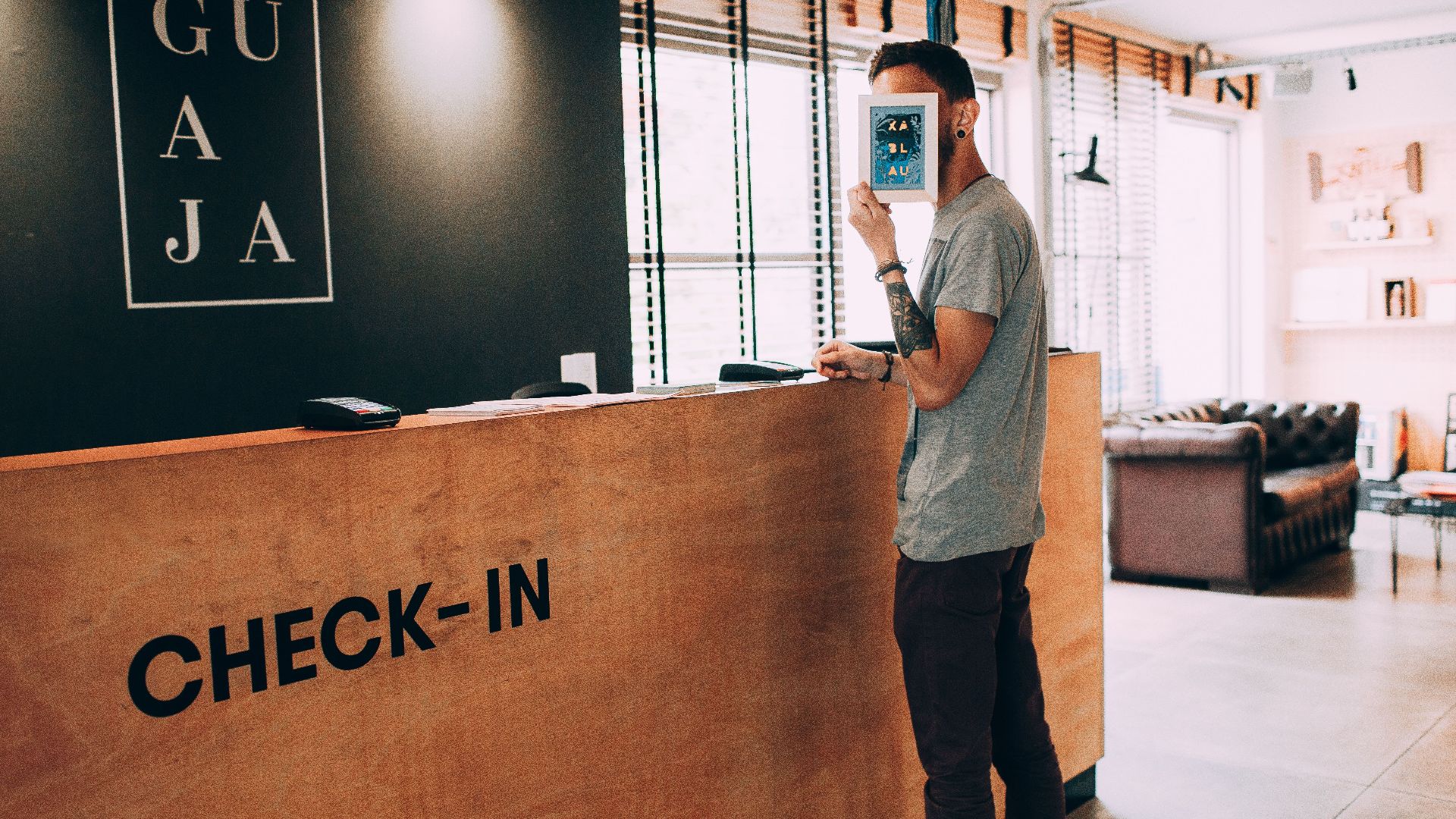 Man standing at a reception desk, holding a book, in a modern hotel lobby.