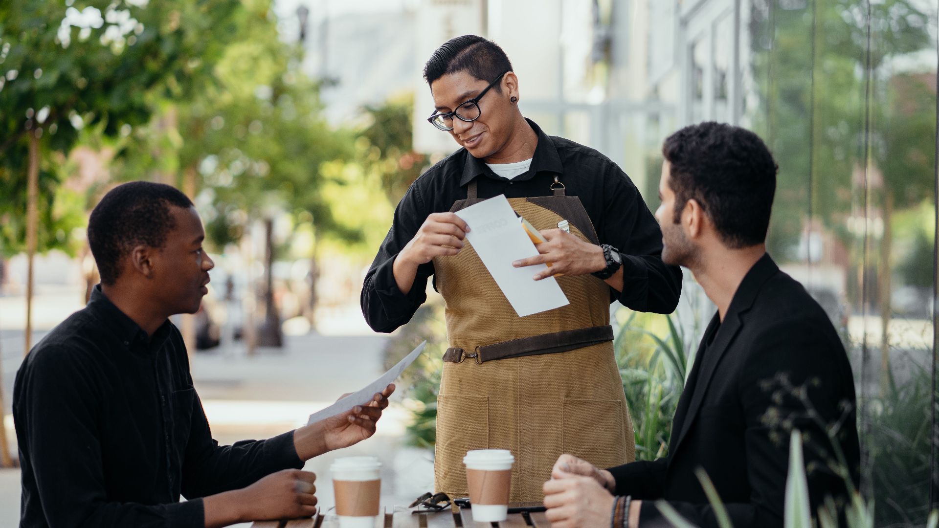 Casual outdoor meeting at a café with diverse friends and friendly waiter.