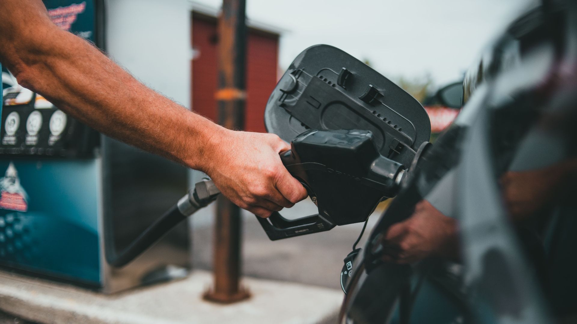 Close-up of a hand holding a nozzle while refueling a car at a gas station.