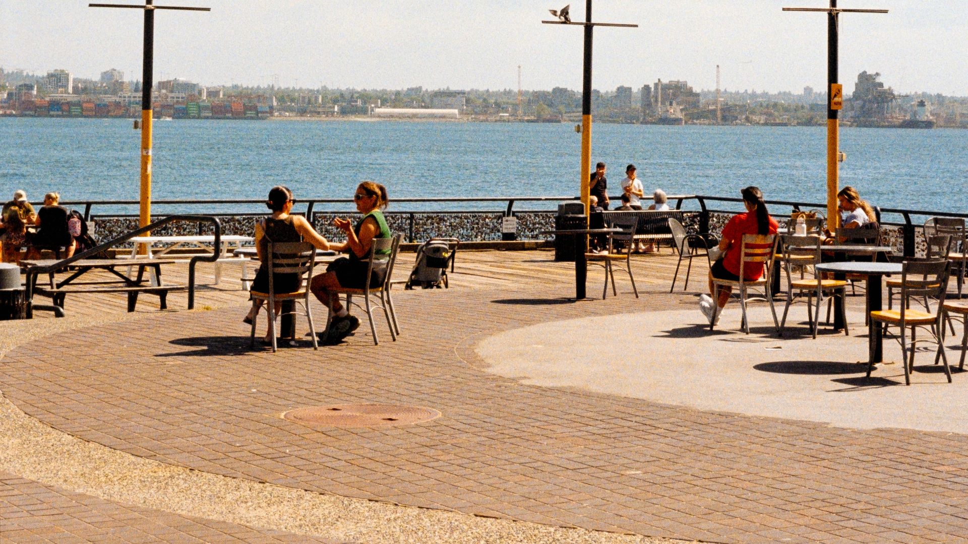 Scenic view of waterfront dining area featuring Canadian and British Columbia flags on a sunny day.