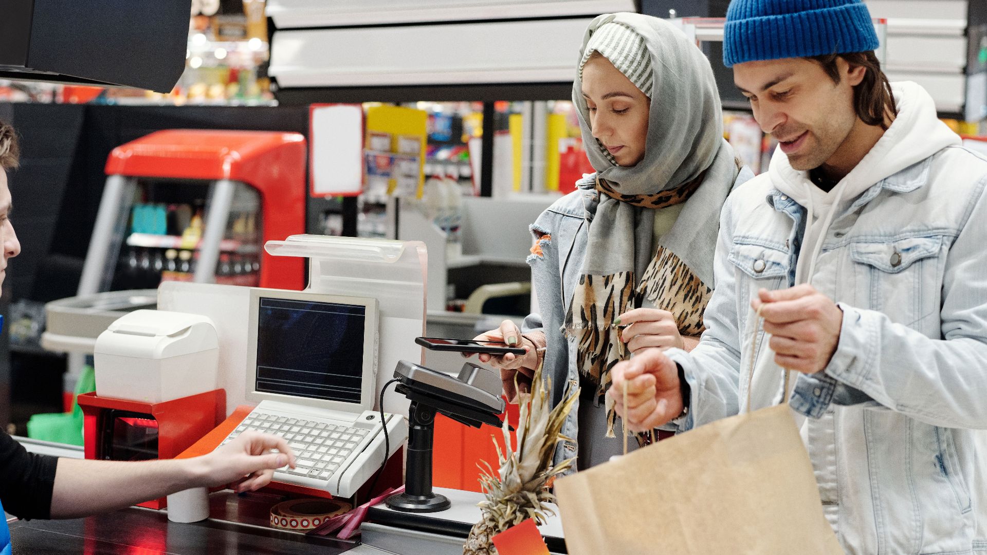 A Middle Eastern couple making a purchase at a supermarket checkout using a smartphone.