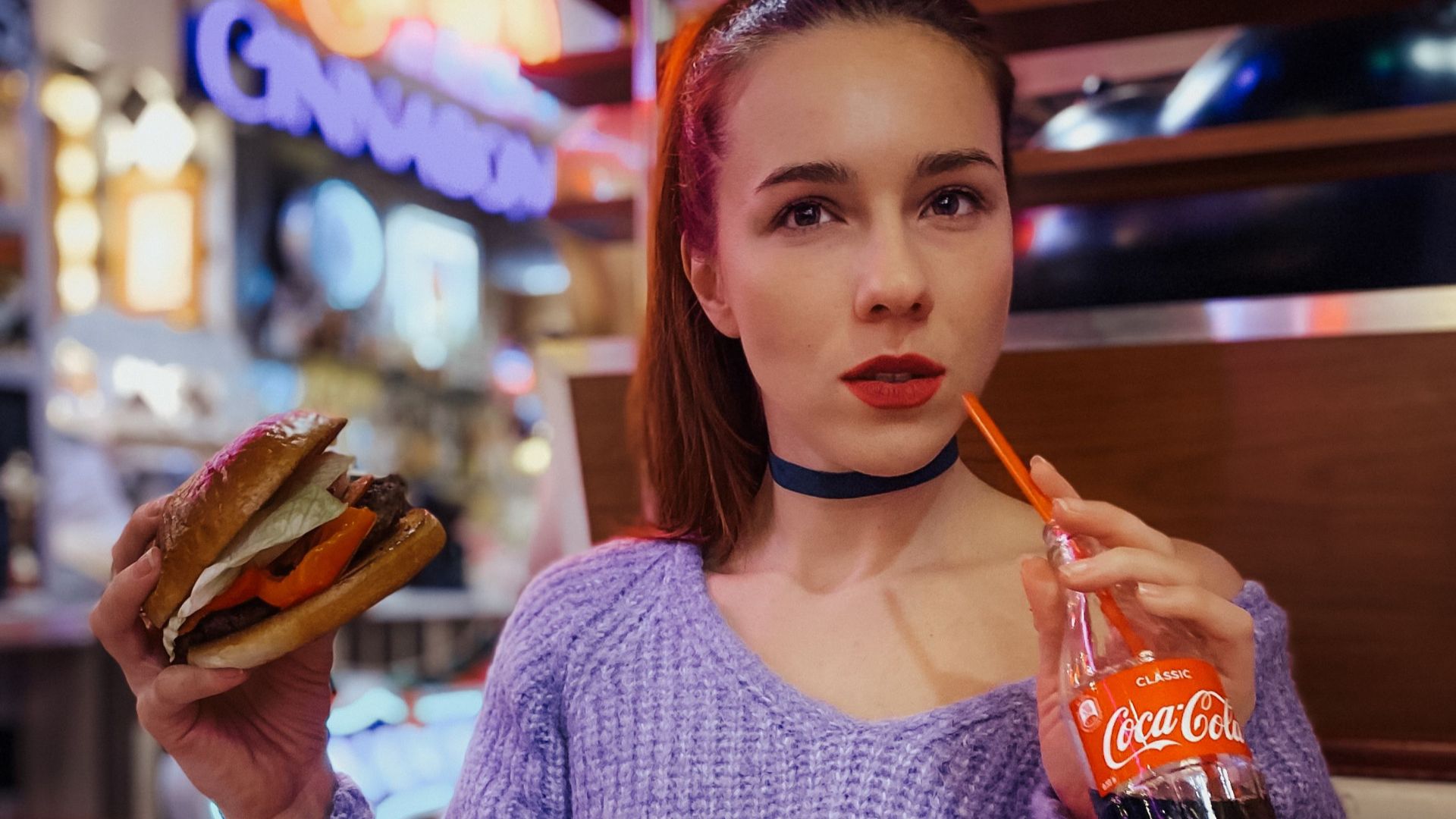 Woman in a retro diner savoring a burger and soda, exuding nostalgia and style.