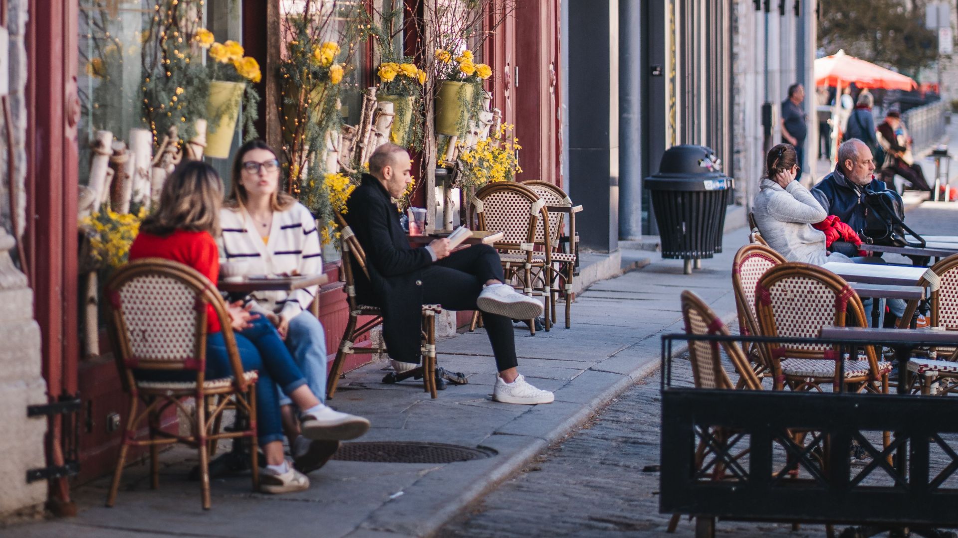 Bustling street scene with a cafe in Old Quebec City, featuring people enjoying a sunny day outdoors.