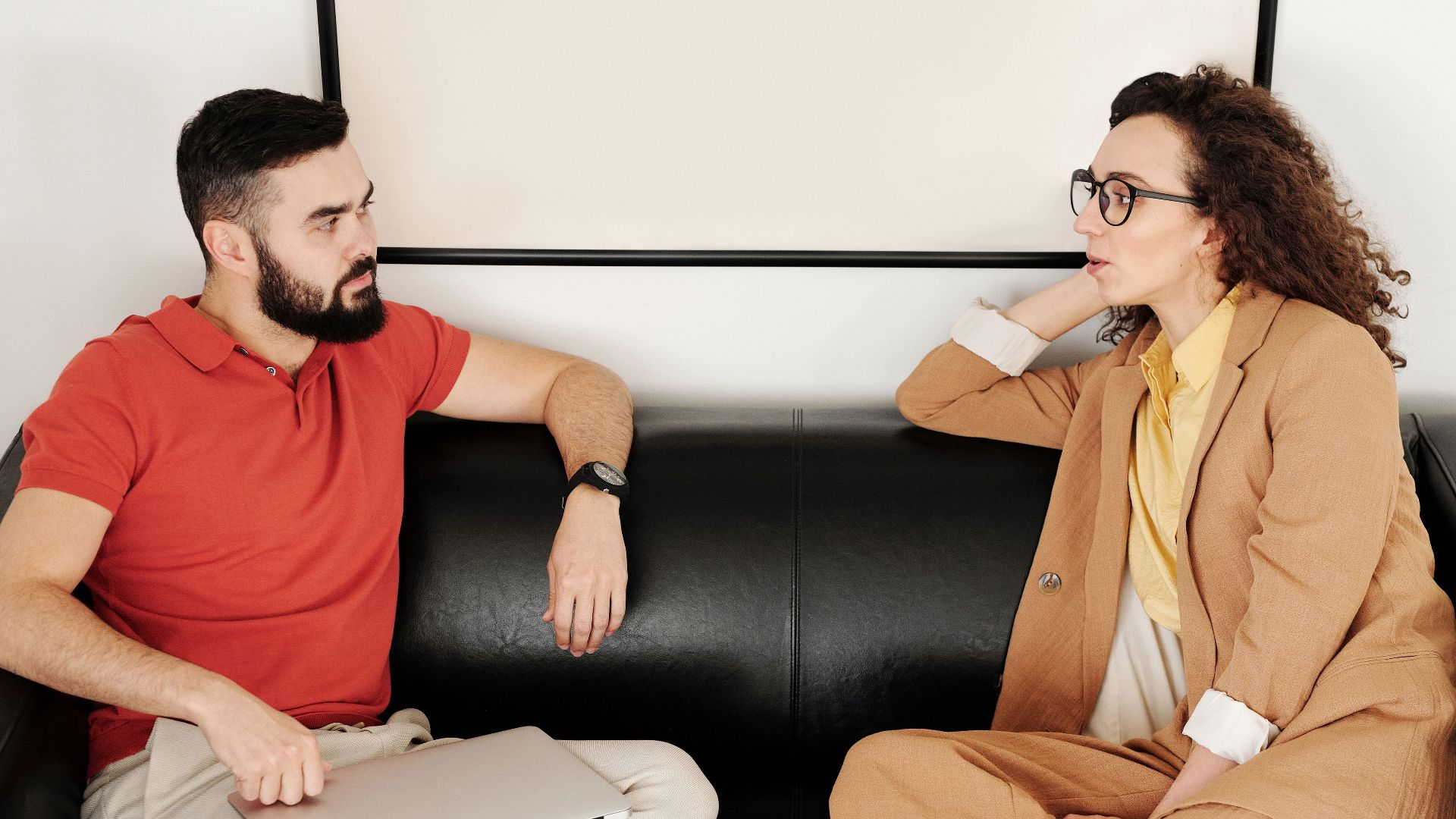 A man and woman sit on a black sofa, having a professional conversation.