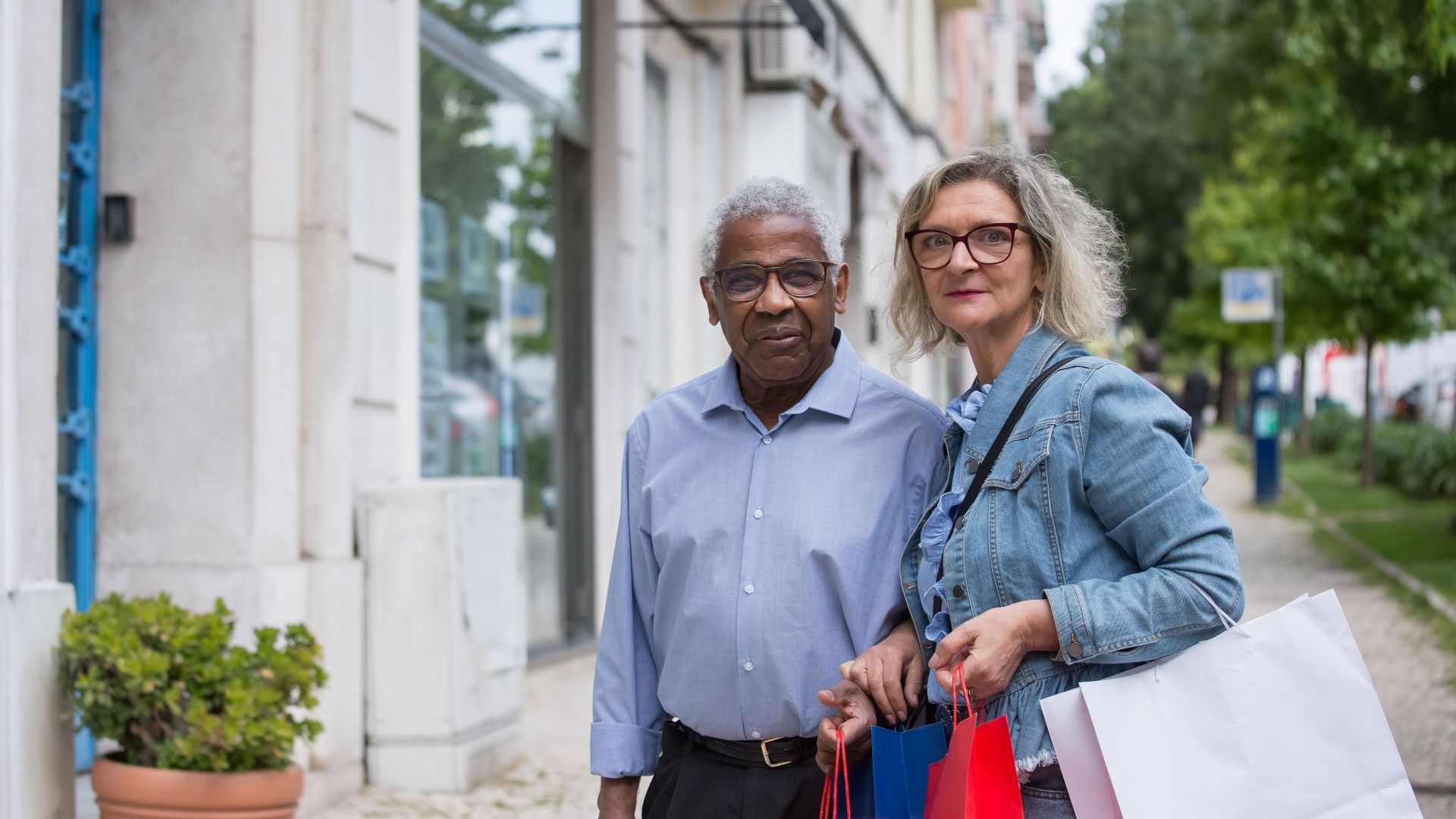 Elderly couple holding shopping bags on a sunny day in Portugal, enjoying leisure time.