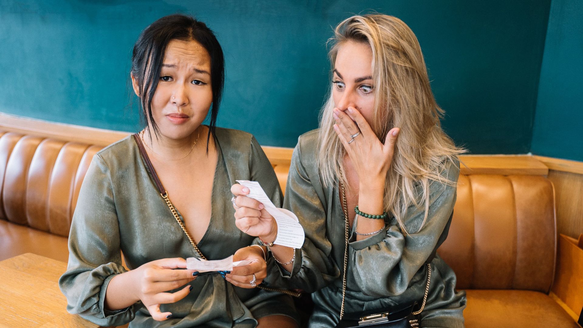 Two women express surprise while reviewing a restaurant bill in a casual setting.