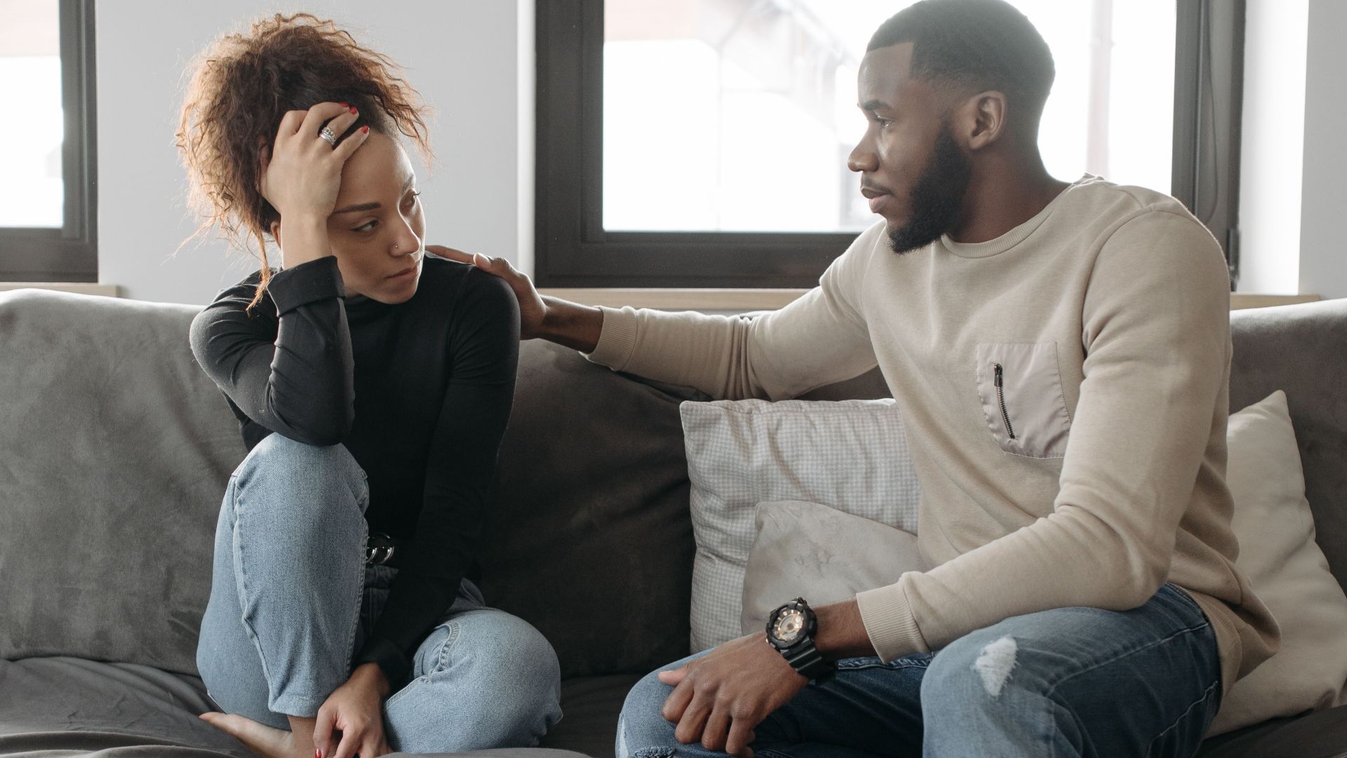 A couple shares a moment on their sofa at home, conveying care and understanding.