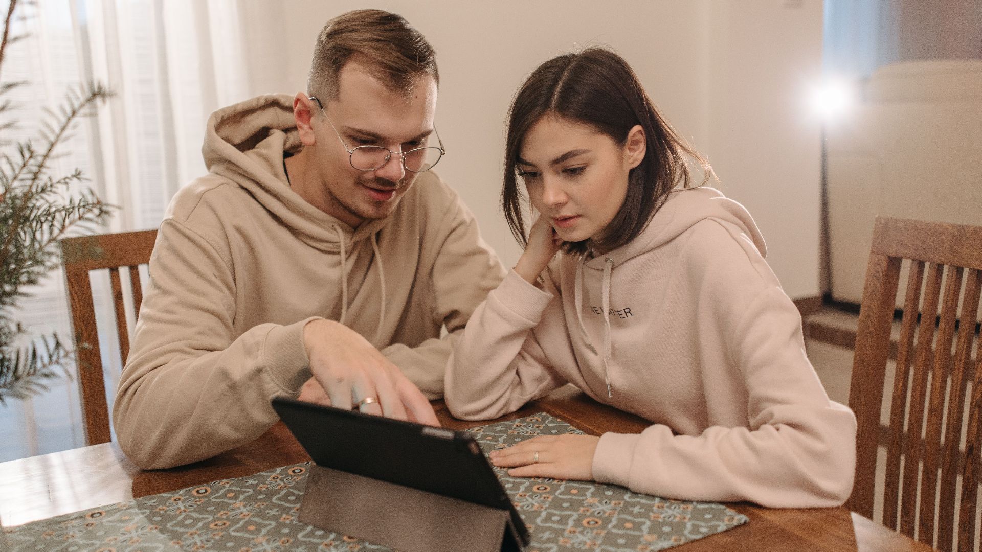 Young couple in hoodies browsing on a tablet together at home.