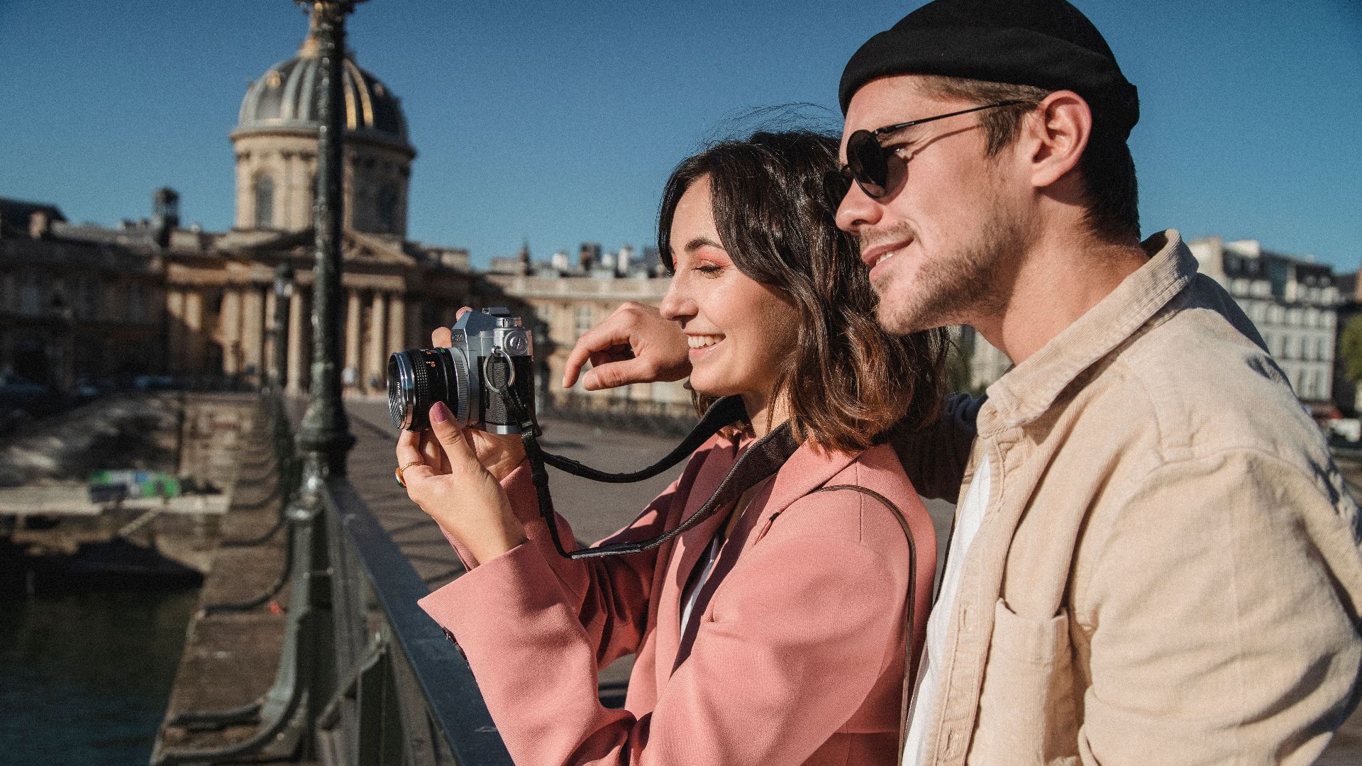 Couple enjoying photography on a Parisian bridge, capturing moments together.