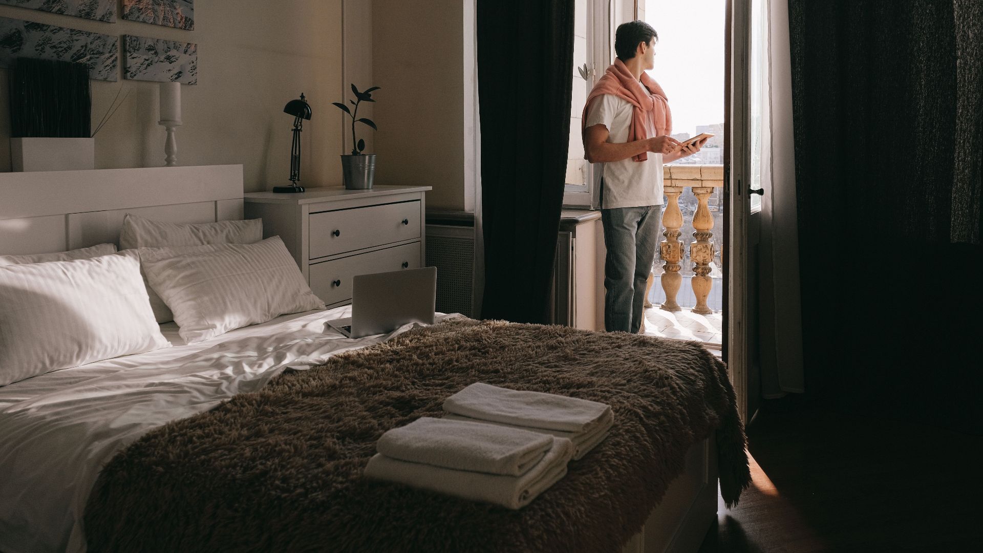 A man stands on a bedroom balcony using a tablet, capturing a moment of relaxation and contemplation.