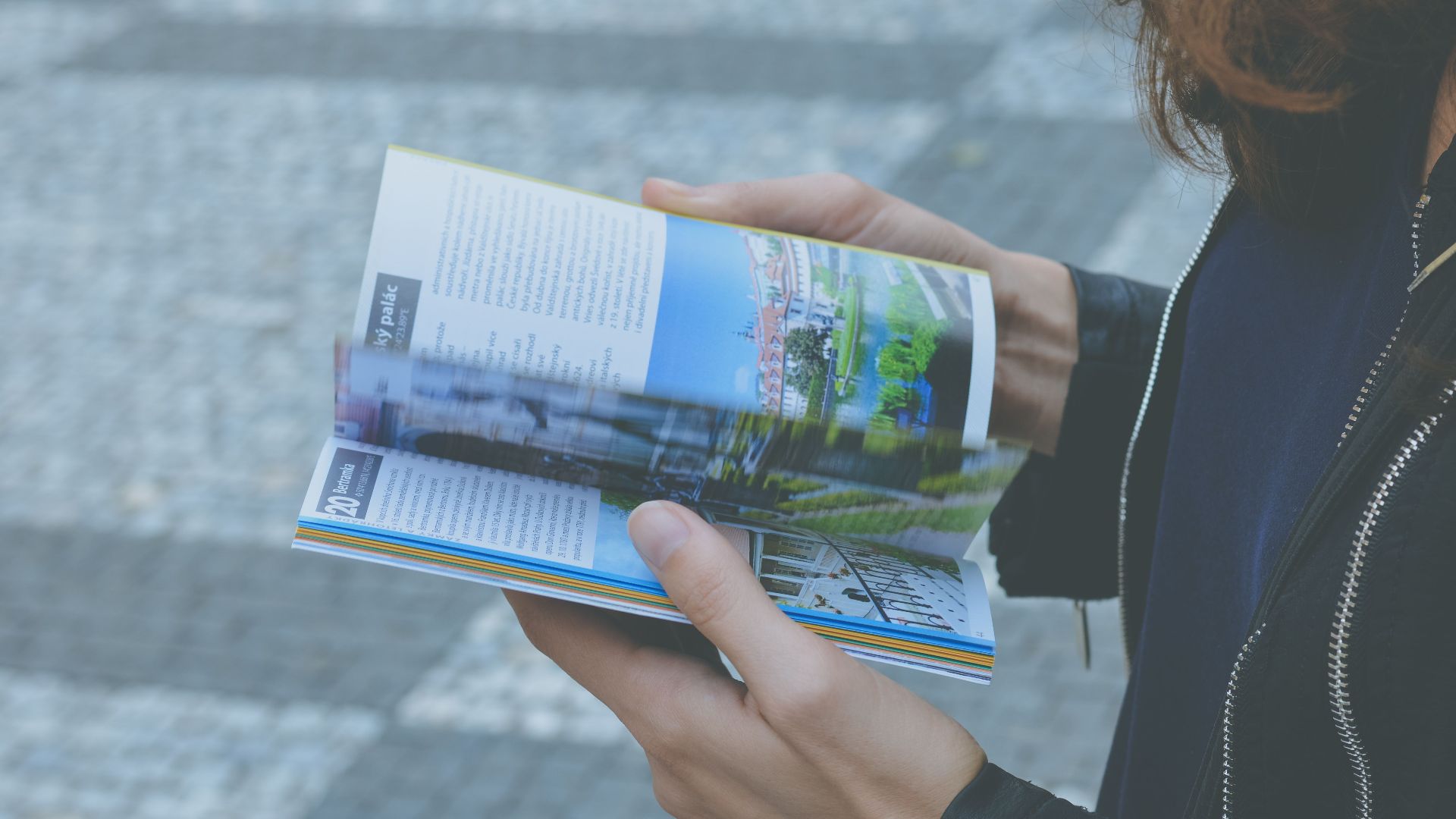 A person flipping through a travel book outdoors, showcasing a variety of vibrant pages.