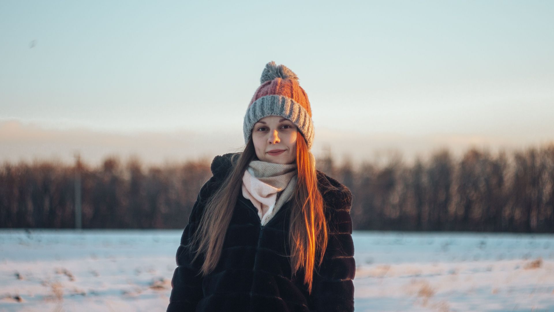 A young woman in winter attire enjoying a sunny day in a snowy landscape.