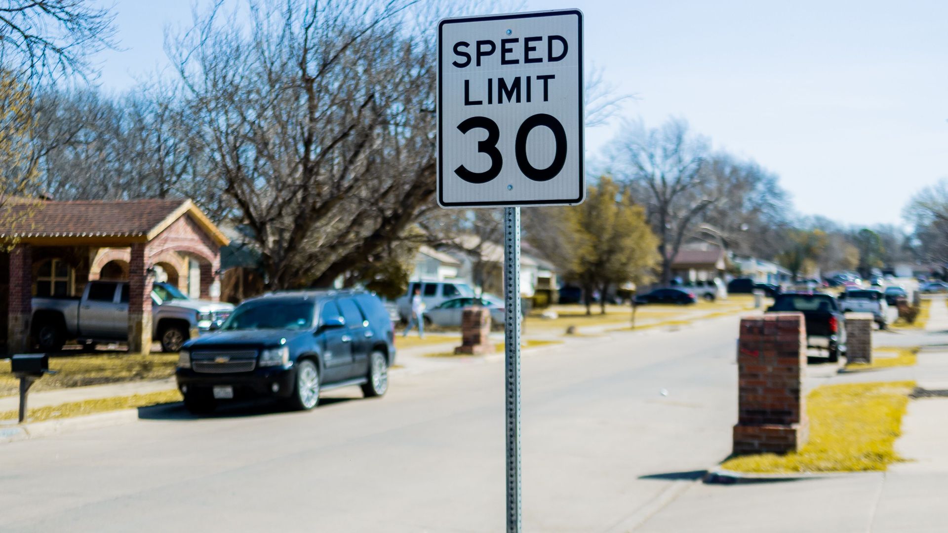 Speed limit 30 sign on a suburban street with cars and houses.