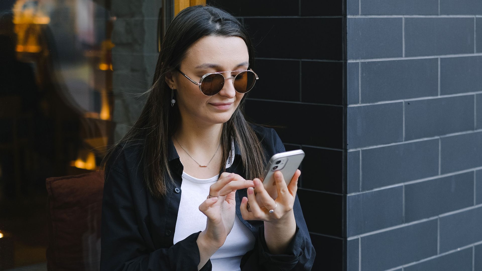 Trendy woman with sunglasses using a smartphone outdoors. Urban lifestyle captured in a candid moment.