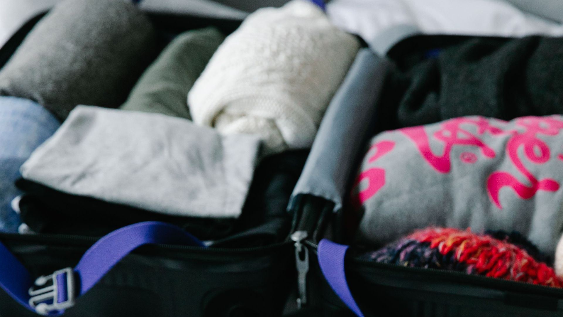A person packs their suitcase with clothes and travel essentials on a bed.