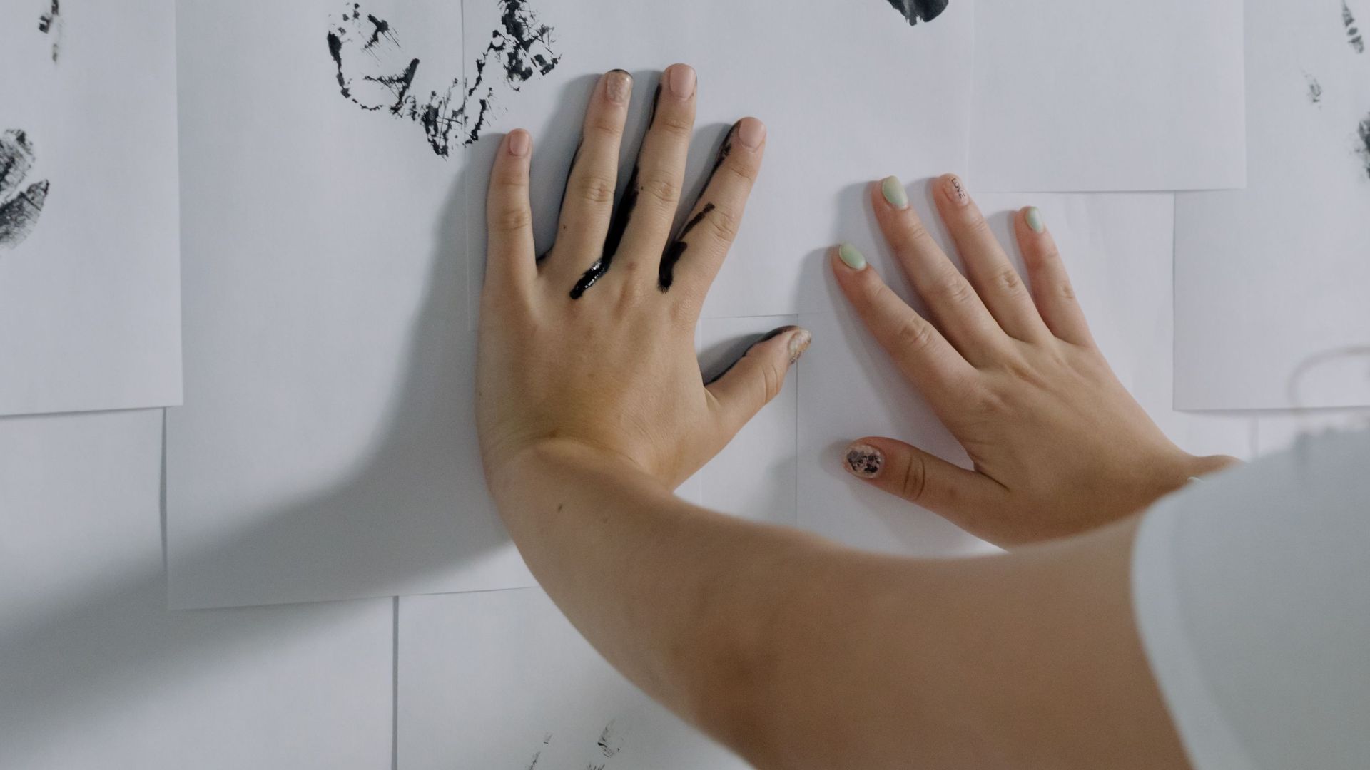 A person arranging white papers with black handprints, creating an artistic display.
