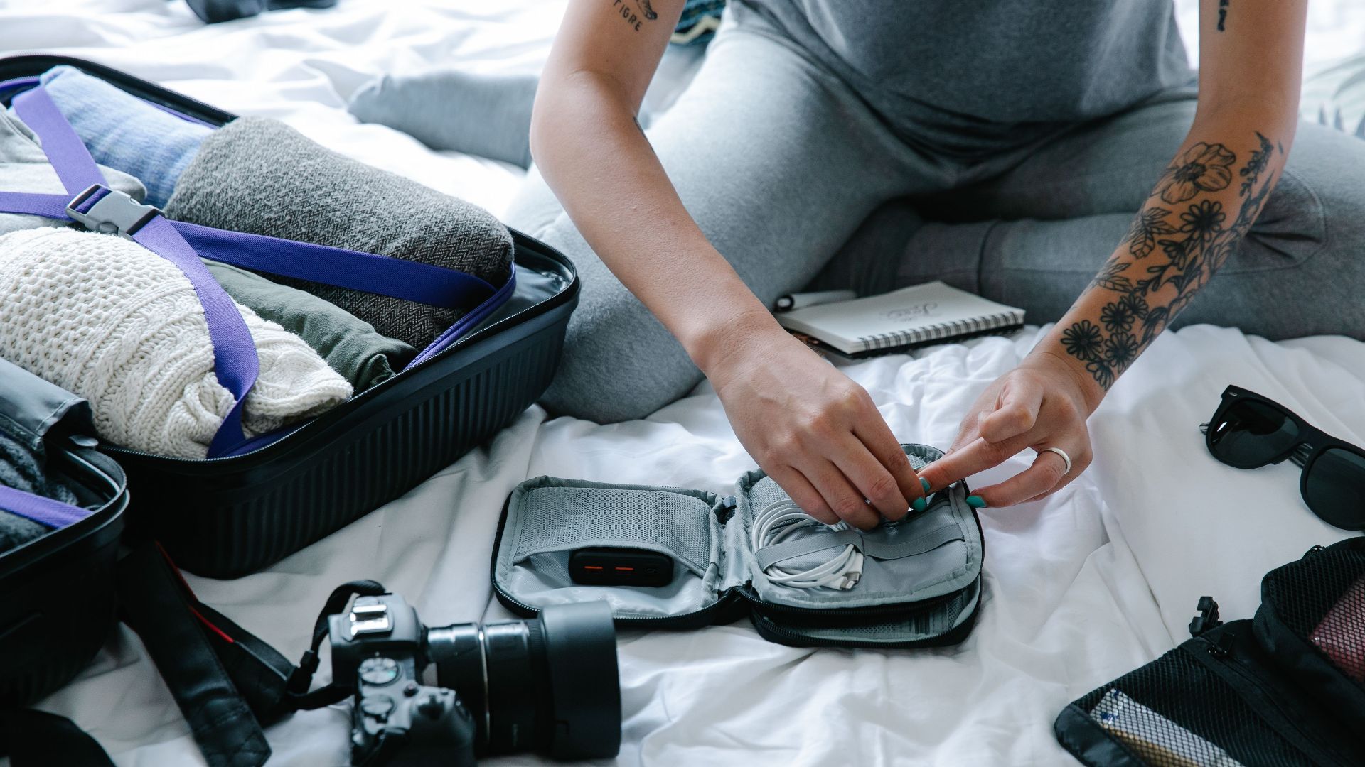 Tattooed woman packs suitcase and tech gadgets, preparing for a trip.
