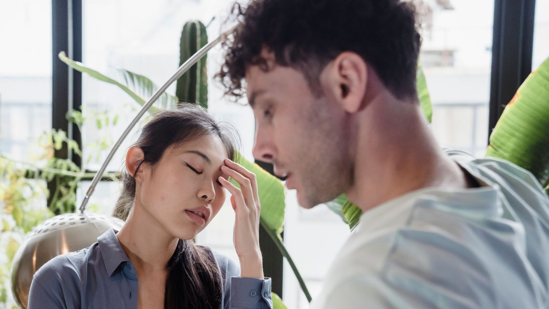 A couple experiencing a tense moment surrounded by plants in a modern space.