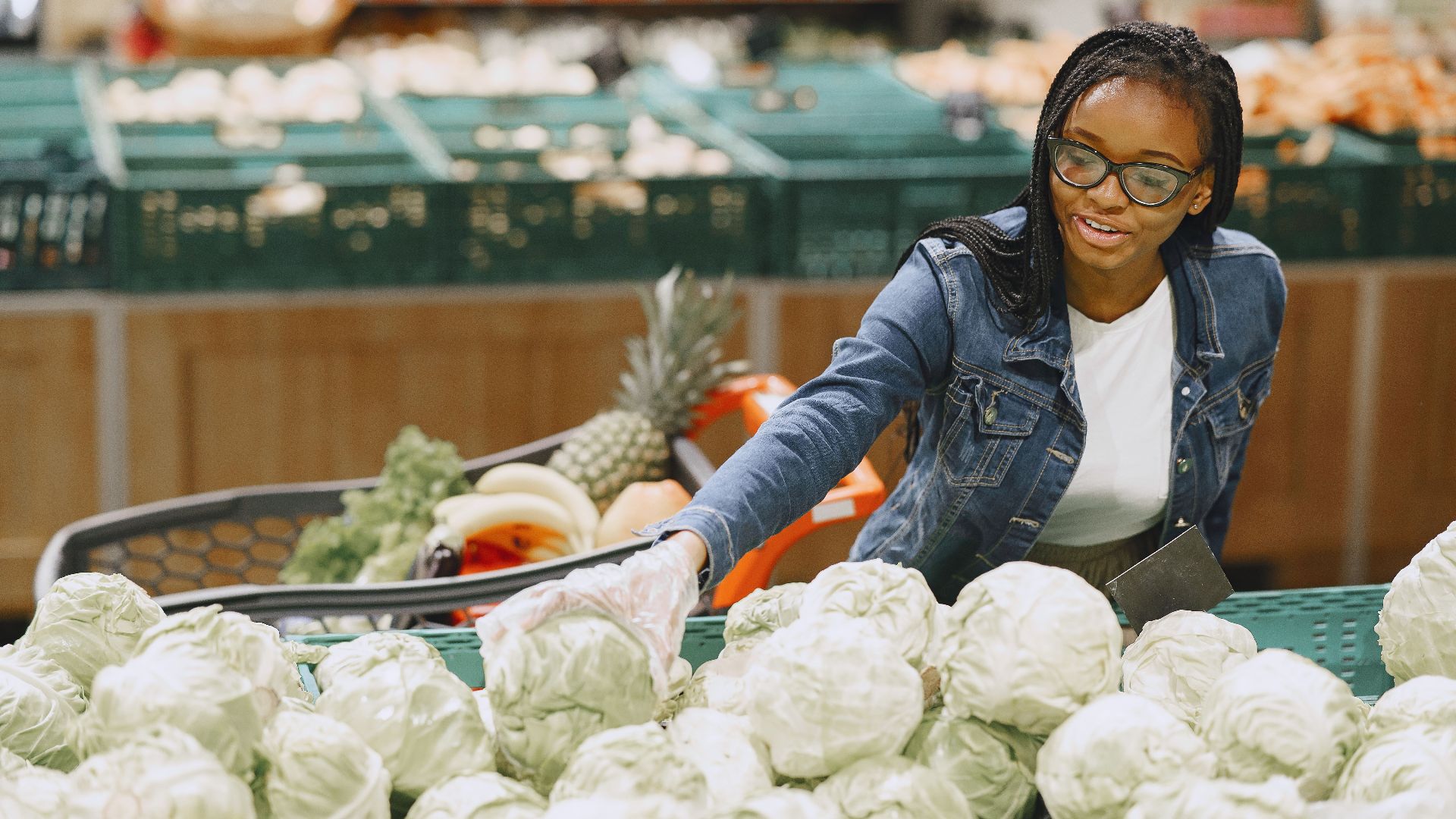 Smiling woman with eyeglasses selecting fresh cabbage at a grocery market.