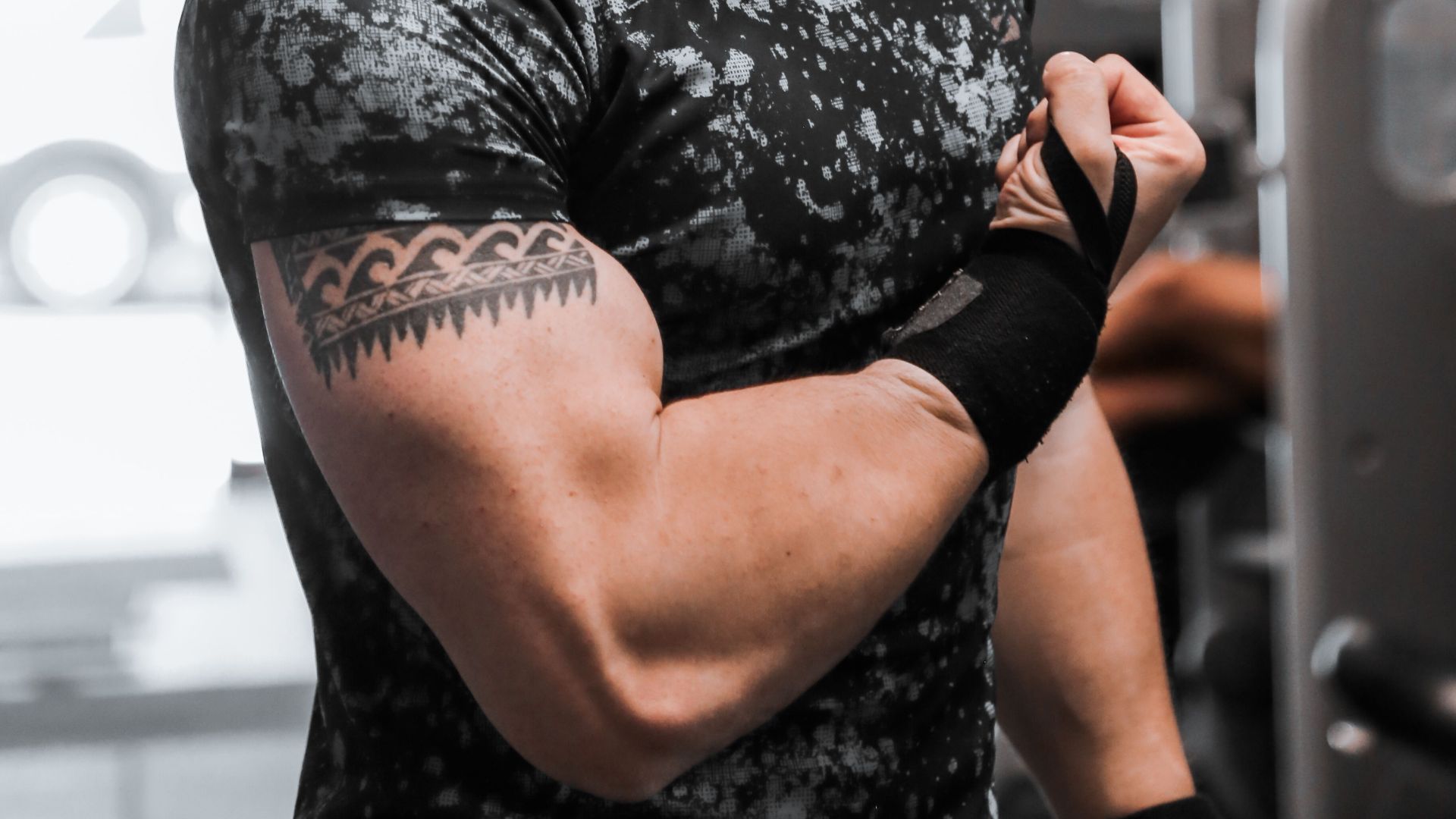 A strong, muscular man flexes his biceps in a gym with modern equipment.
