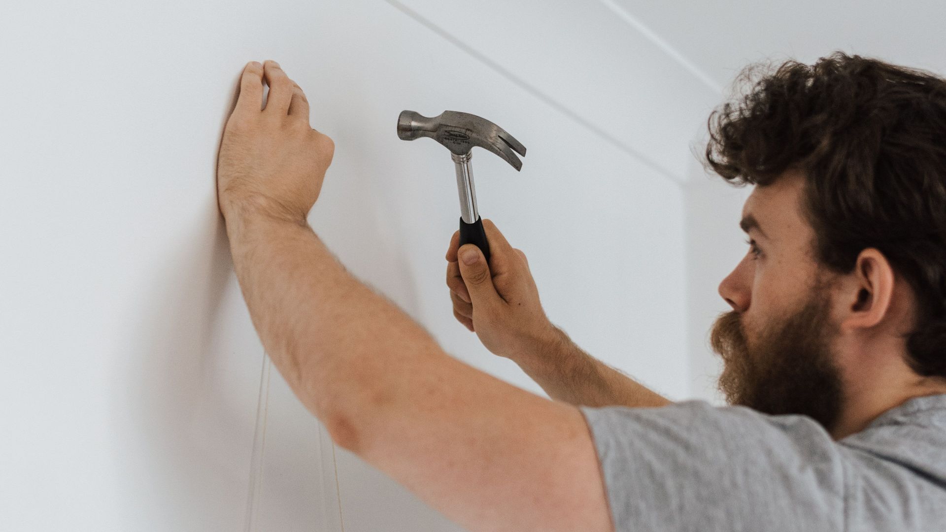 Side view of bearded craftsman with hammer putting decoration on wall during renovation works