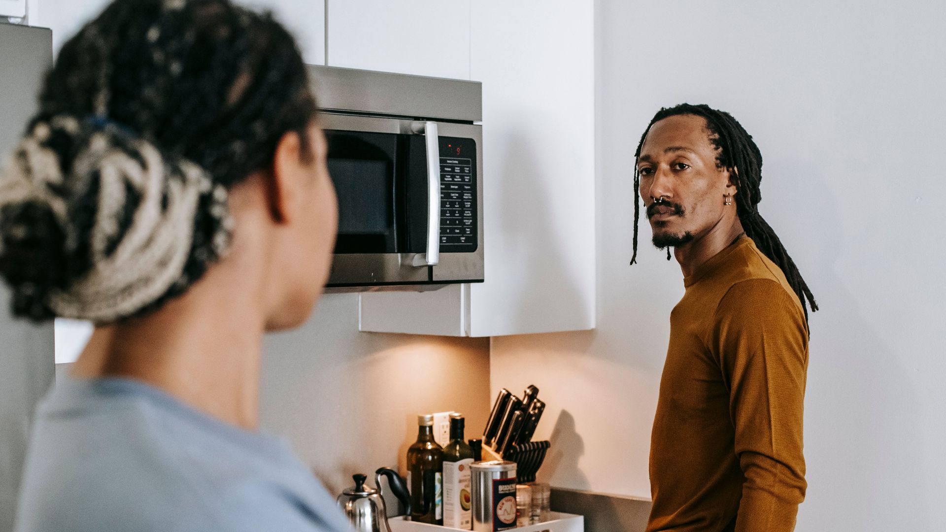 Anonymous ethnic female speaking with boyfriend with dreadlocks while looking at each other in house