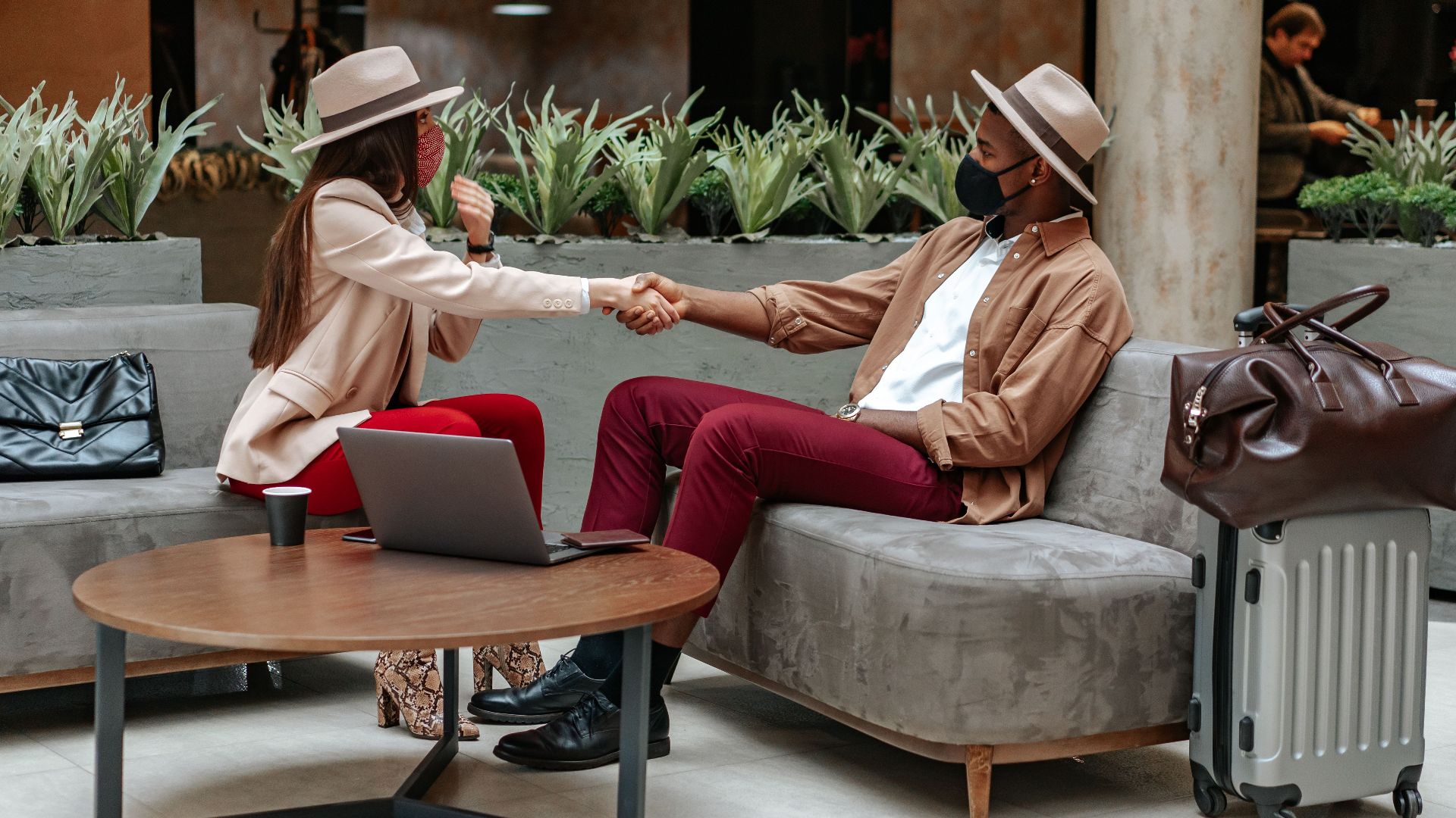Two fashionable individuals shaking hands in a hotel lobby, showcasing travel and safety.