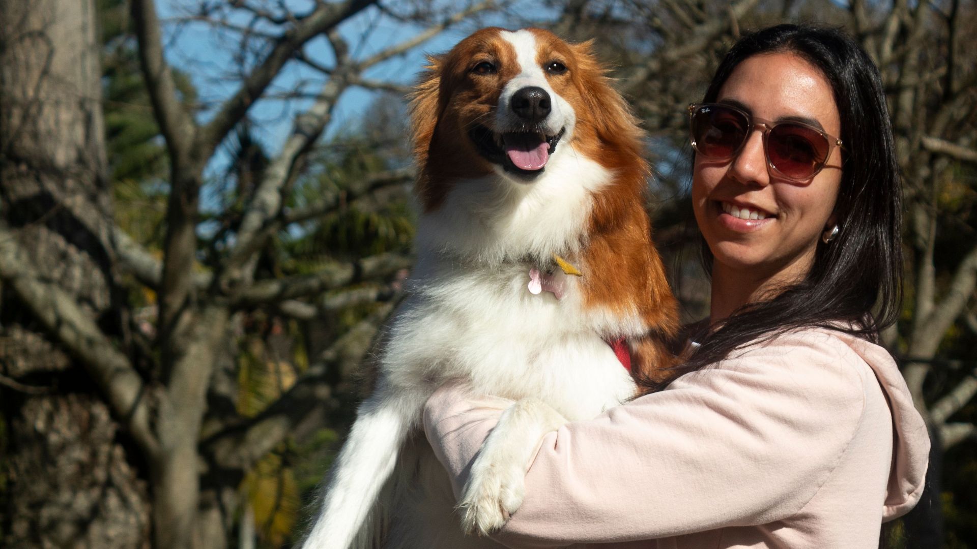 A cheerful woman holds a happy dog in a sunlit park in Montevideo, Uruguay.