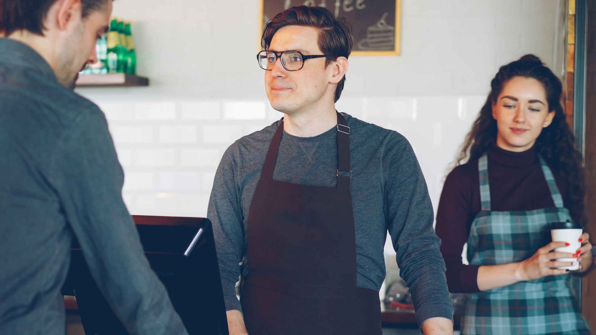 Casual interaction at a coffee shop counter with barista and customers.
