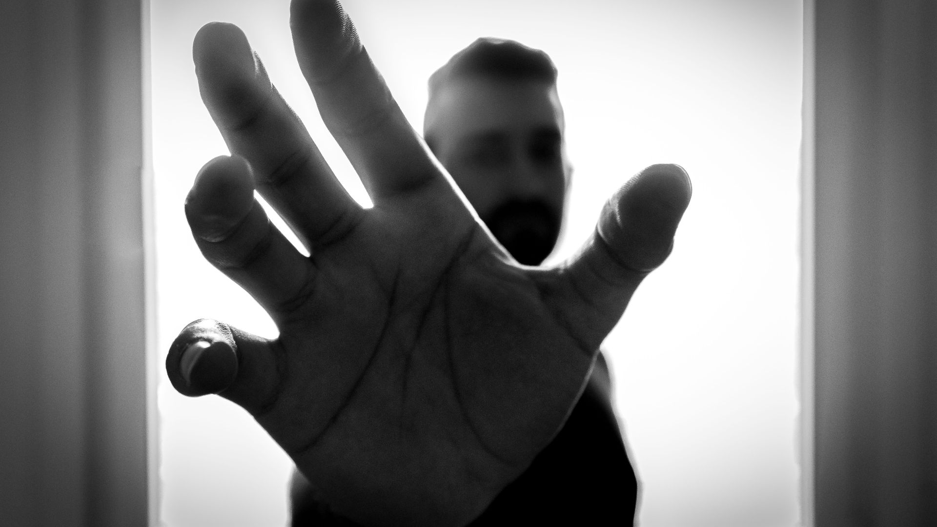 Black and white close-up of hand reaching out with blurred figure in background.