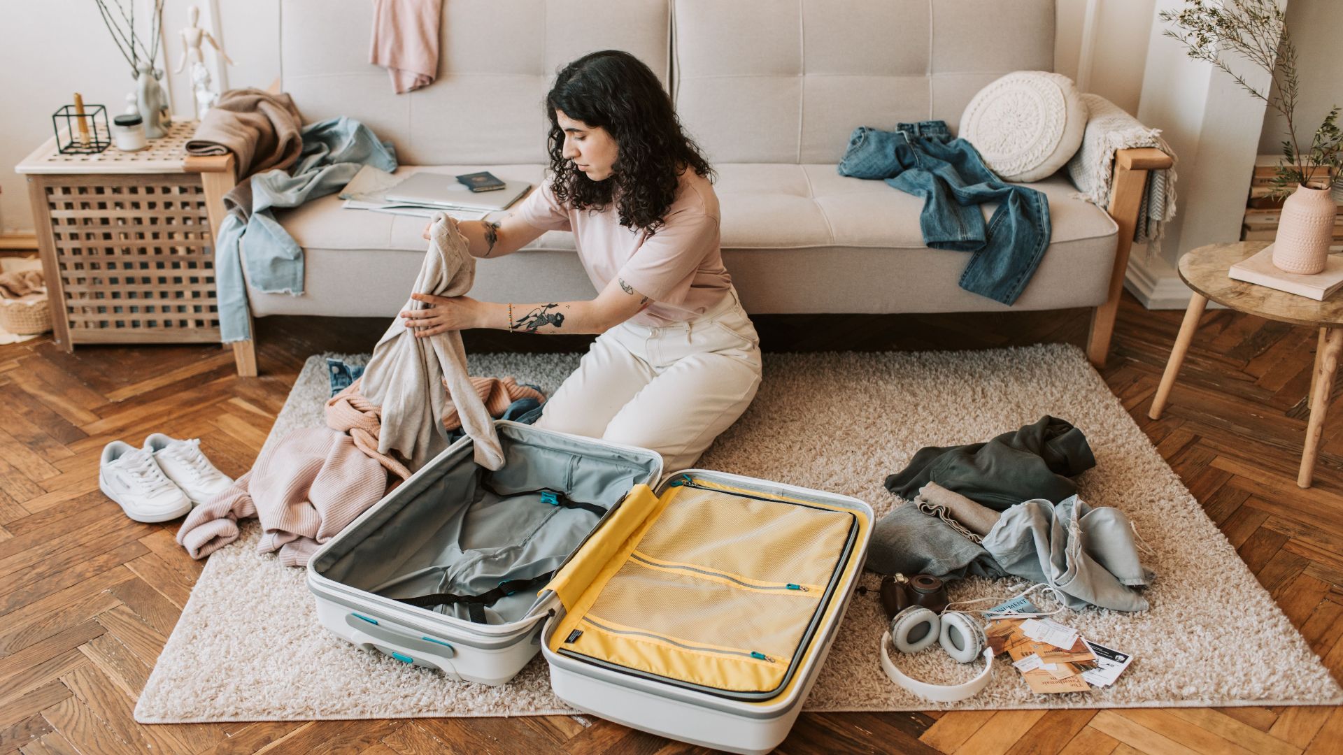 Woman organizing clothes in a suitcase while preparing for a trip in a stylish living room.