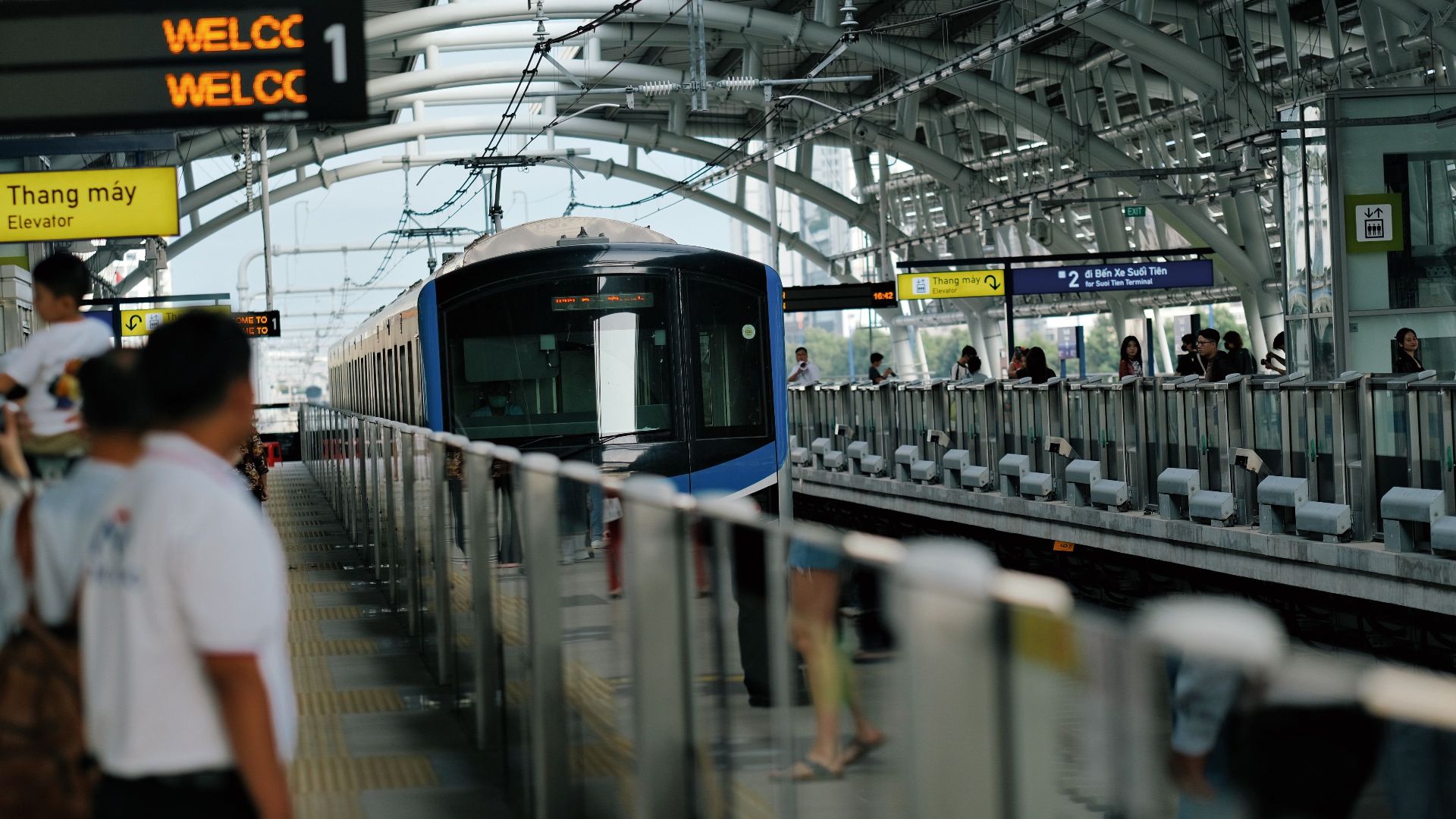 Dynamic scene at a modern metro station in Vietnam, featuring a moving train and diverse commuters.
