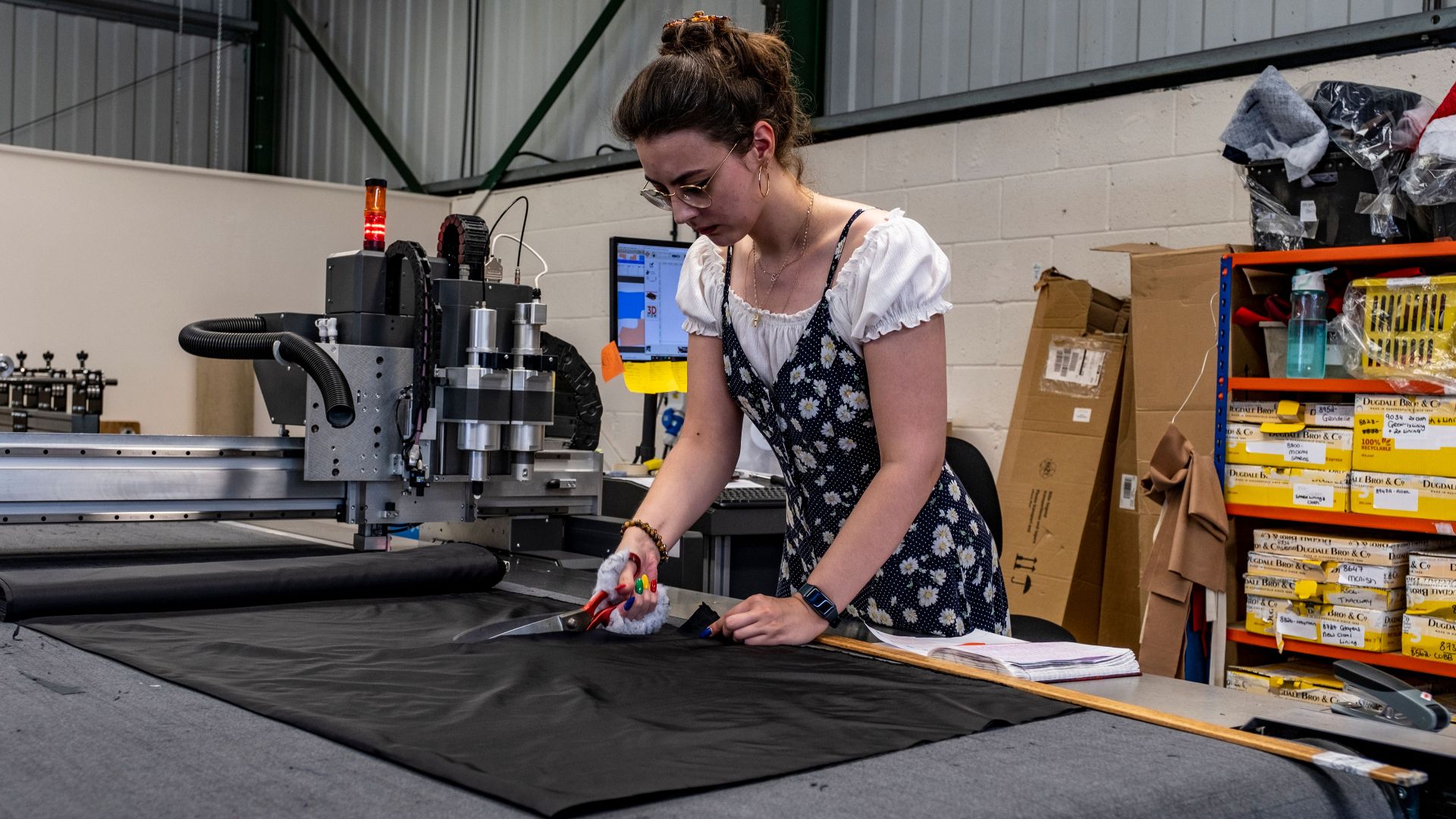 Female tailor cutting fabric in a factory environment, demonstrating precision and craftsmanship.