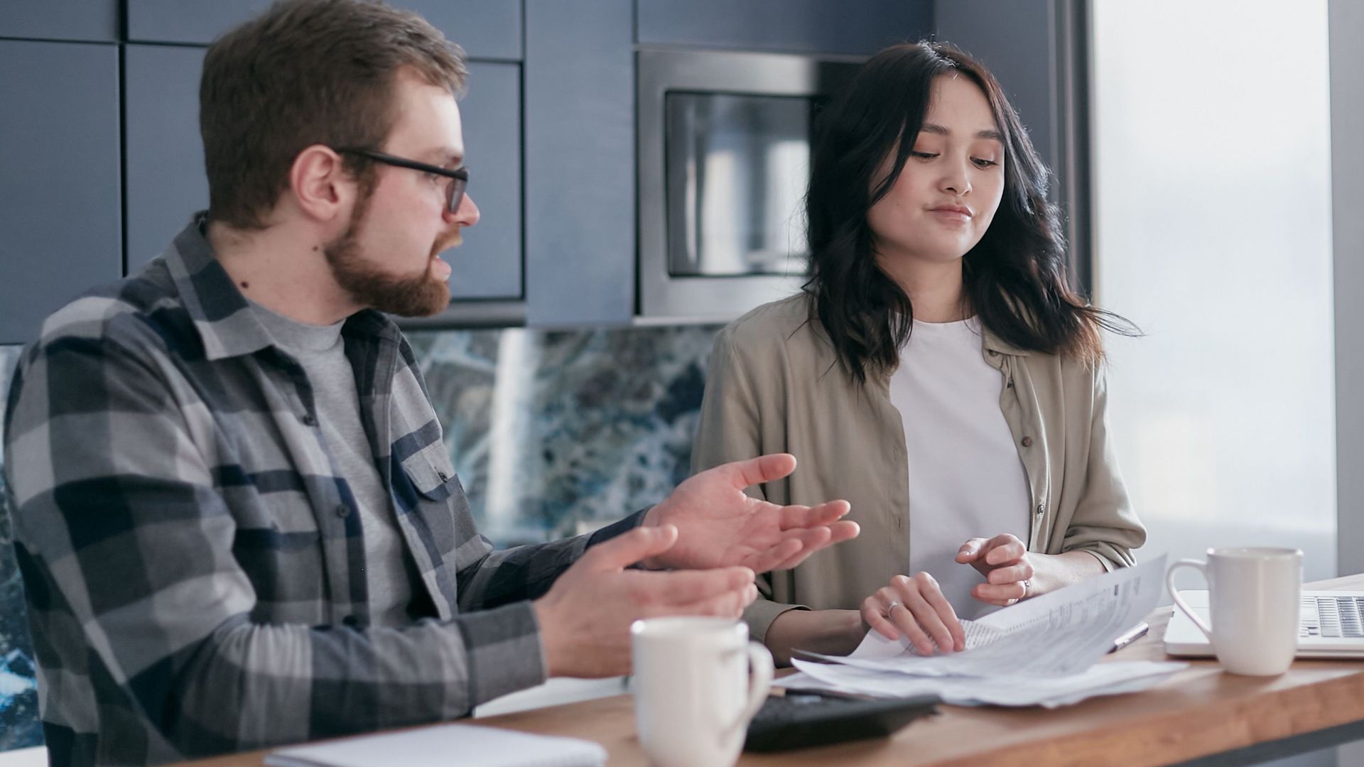 A couple reviewing financial documents in their kitchen, appearing focused and concerned.