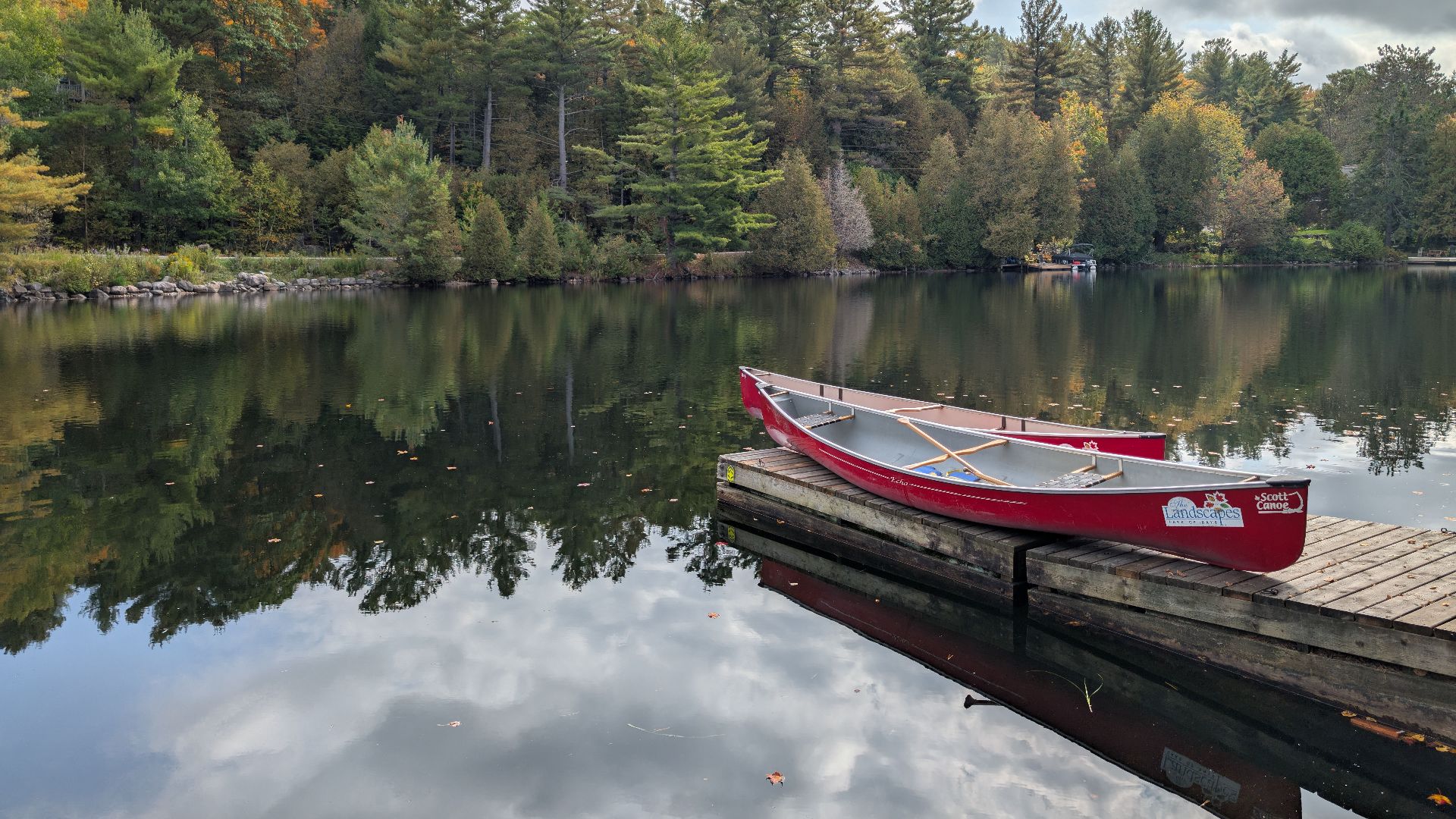 A tranquil scene of a red canoe on a dock by a reflective lake surrounded by lush forest.